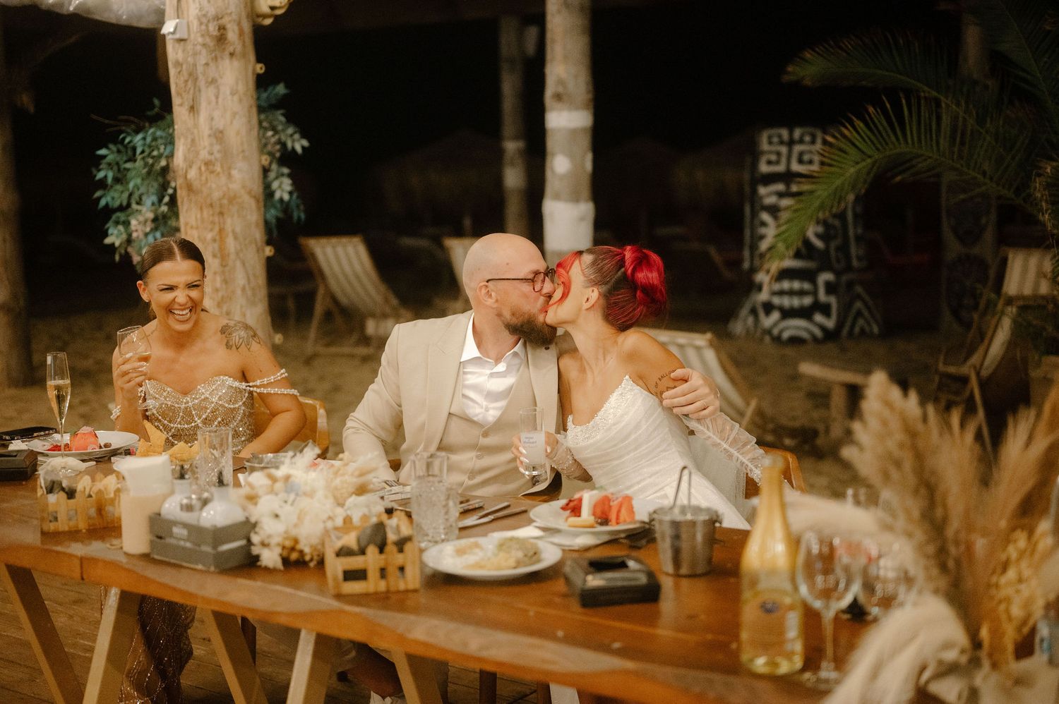 A group of people enjoying an outdoor dinner party at a long table decorated with pampas grass centerpieces.