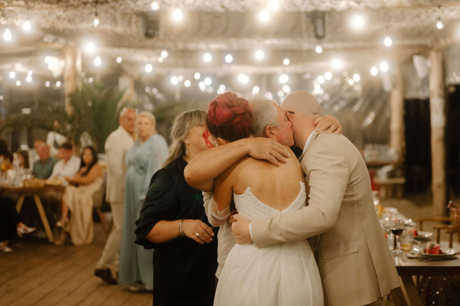 A romantic outdoor wedding reception under string lights with guests seated at long tables during twilight hours.