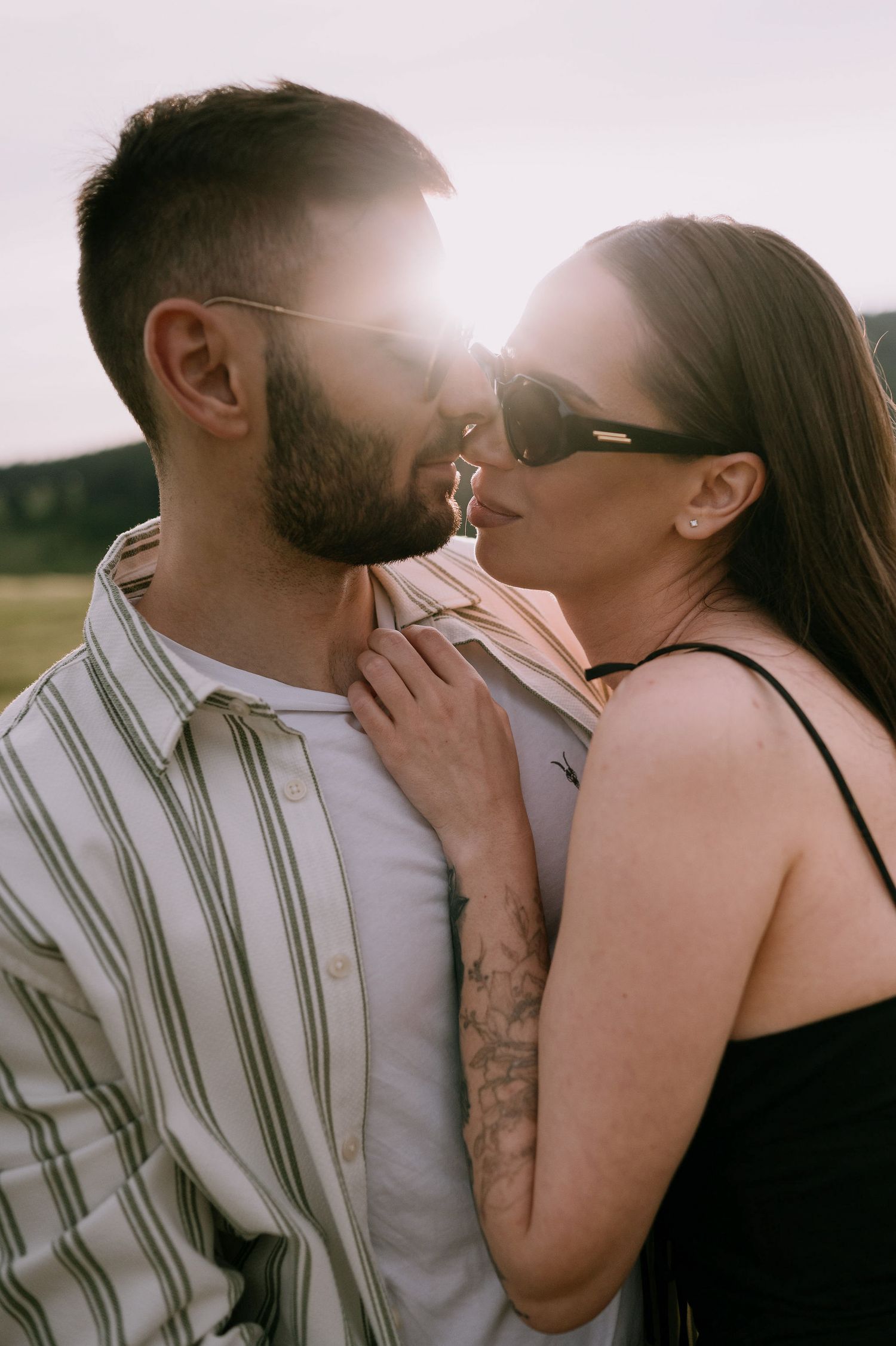 Romantic couple sharing tender kisses in a sunlit field with soft lighting and intimate poses.
