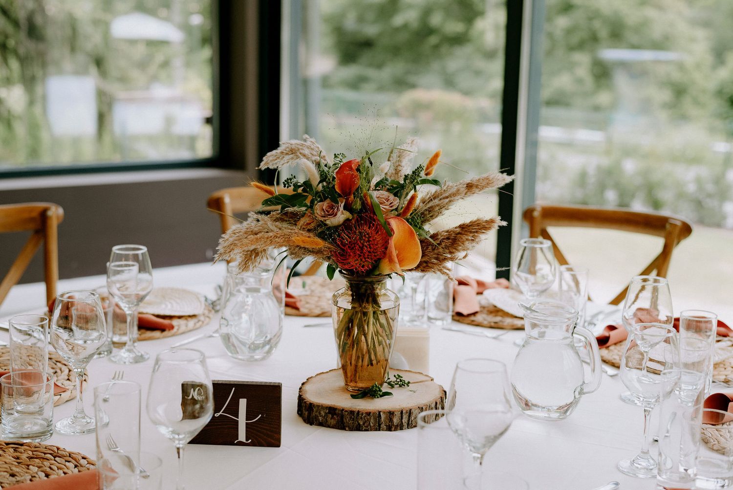 Elegant wedding reception table settings with wine glasses and rustic wood slice centerpieces in natural lighting.