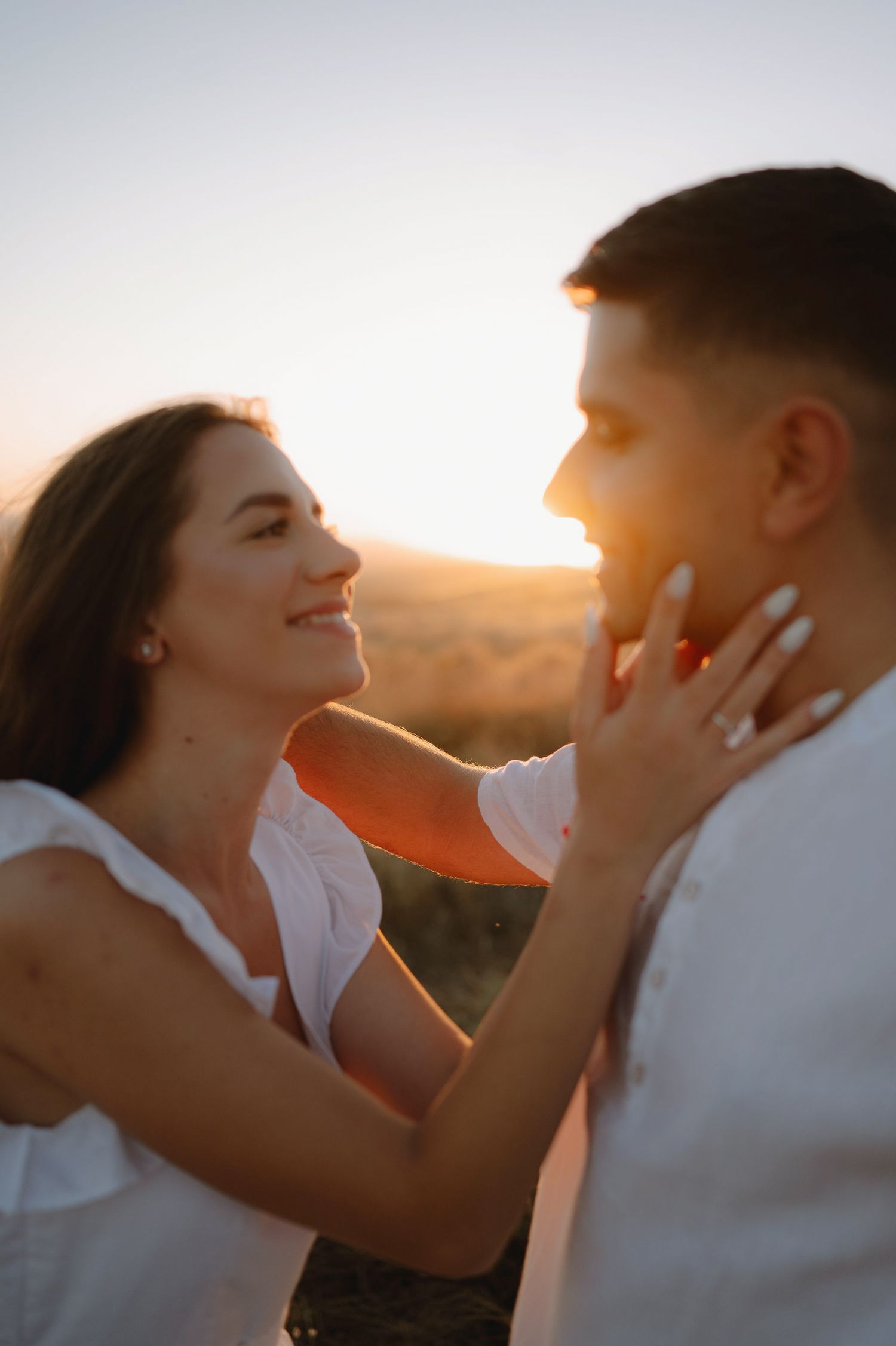 Romantic couple embraces in warm golden sunlight during sunset photoshoot.