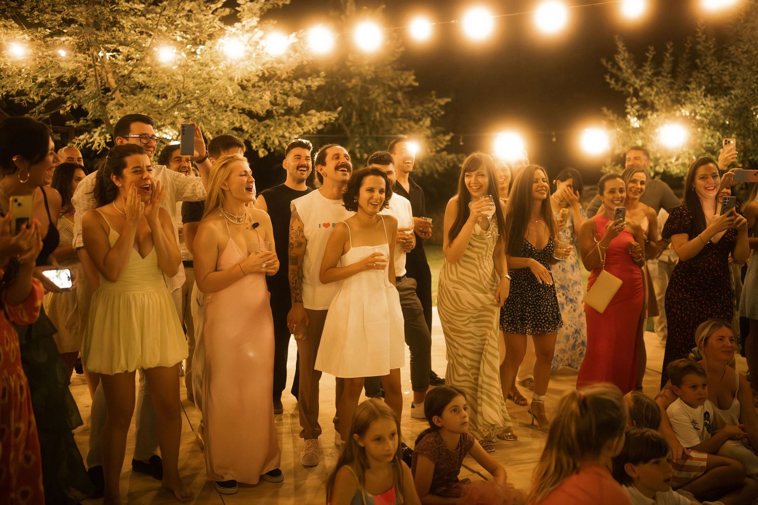 Guests dancing and celebrating at an outdoor evening wedding reception under warm string lights.