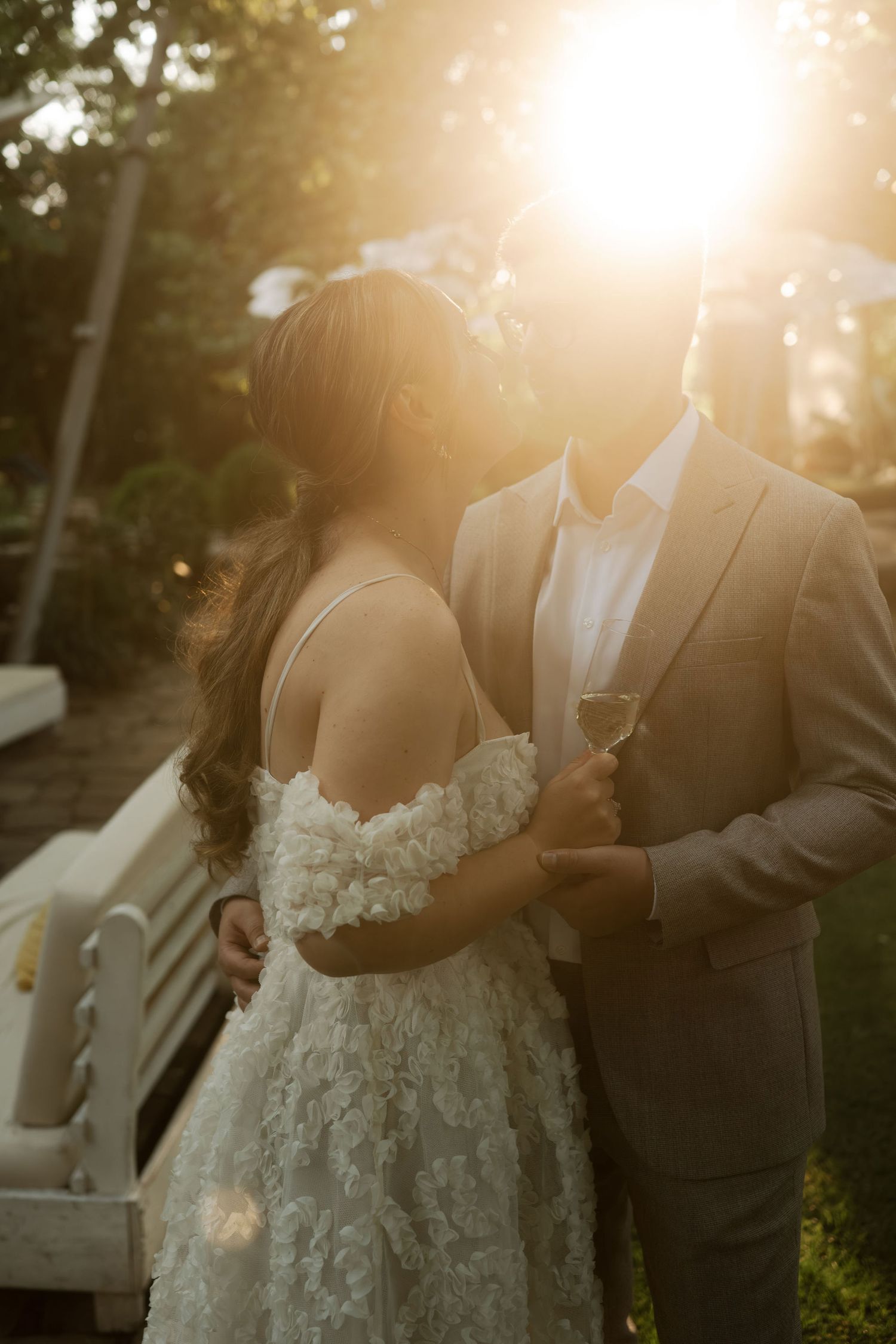 A couple shares an intimate moment at sunset during their wedding ceremony, with golden sunlight streaming through trees.