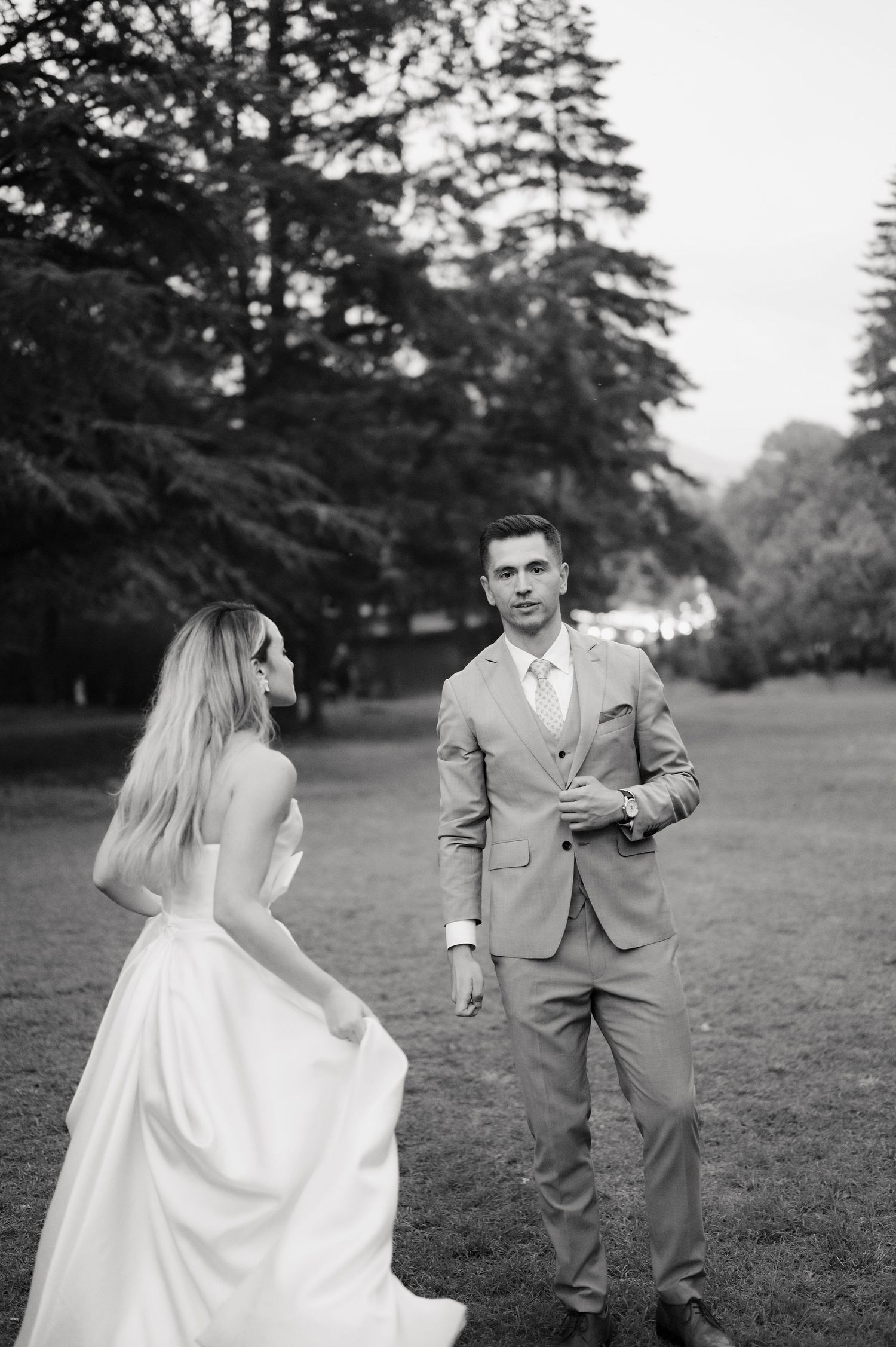 A couple shares a playful moment during their outdoor wedding photoshoot in a grassy field with tall trees.