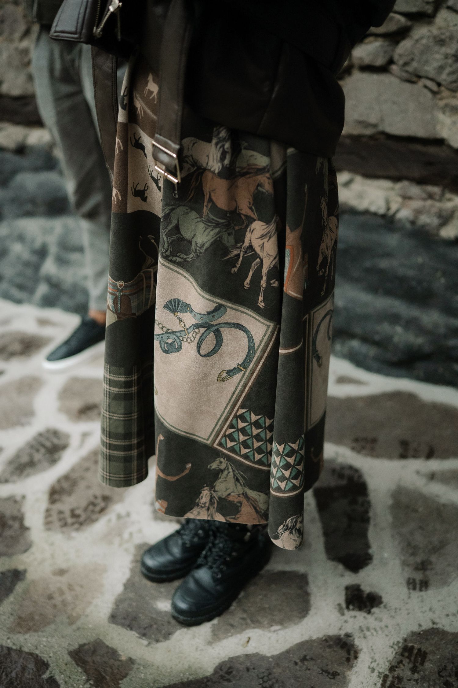 Close-up view of black boots and patterned fabric against a snowy ground surface.