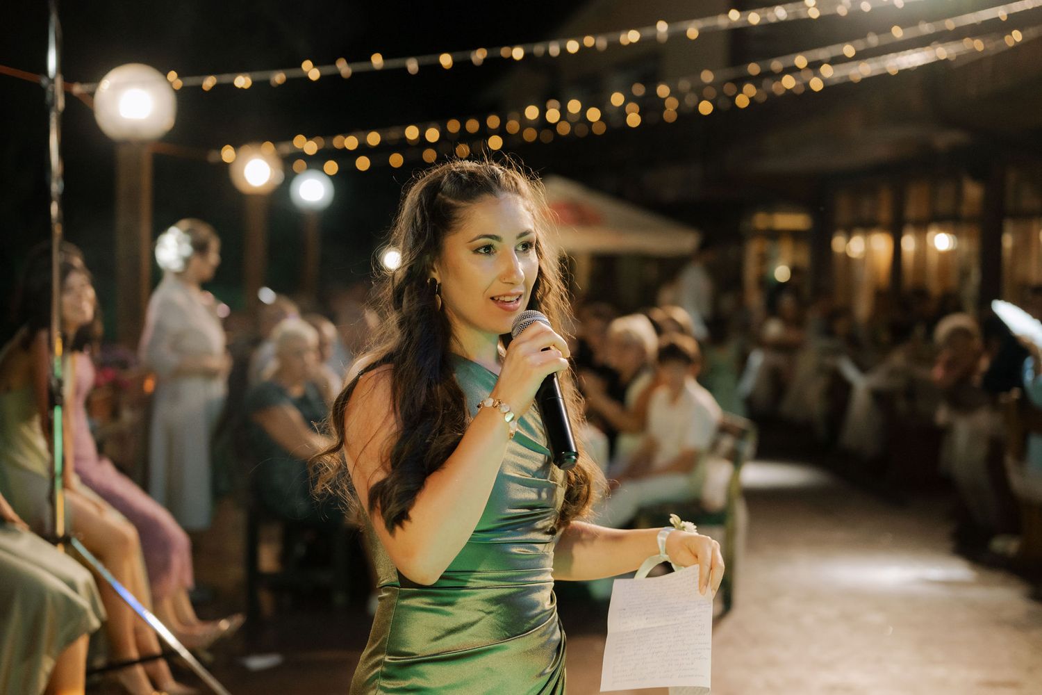 String lights illuminate an outdoor evening wedding reception with guests mingling and dancing on the patio.