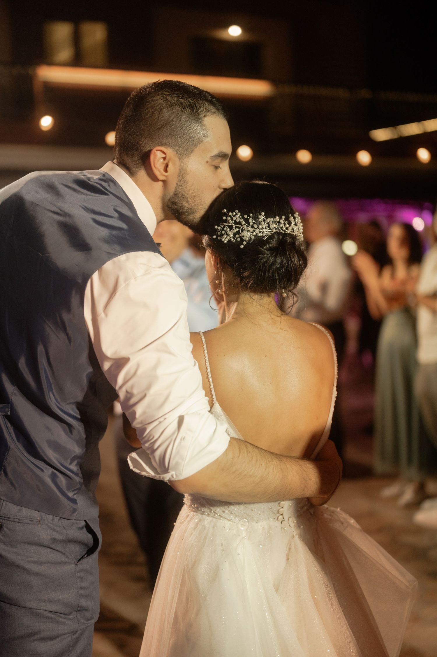 A couple shares a romantic dance at their wedding reception as guests look on in the background.
