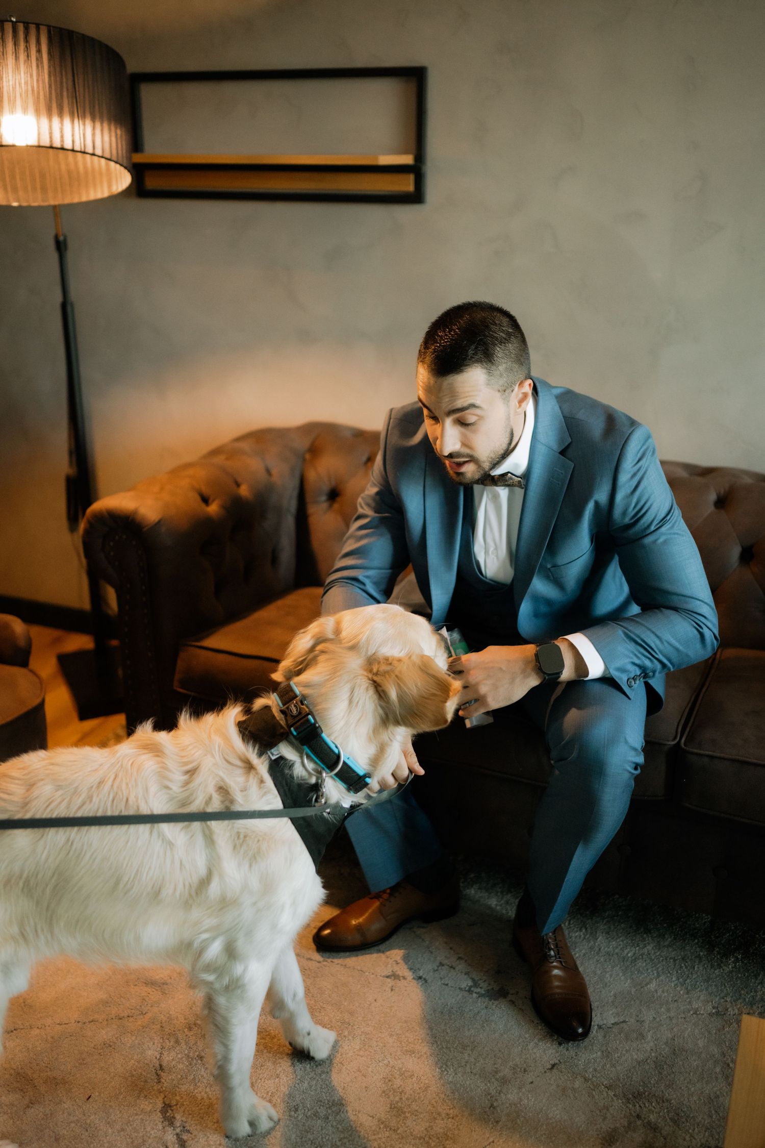 Person in blue suit affectionately petting and interacting with a fluffy white dog in a dimly lit room.