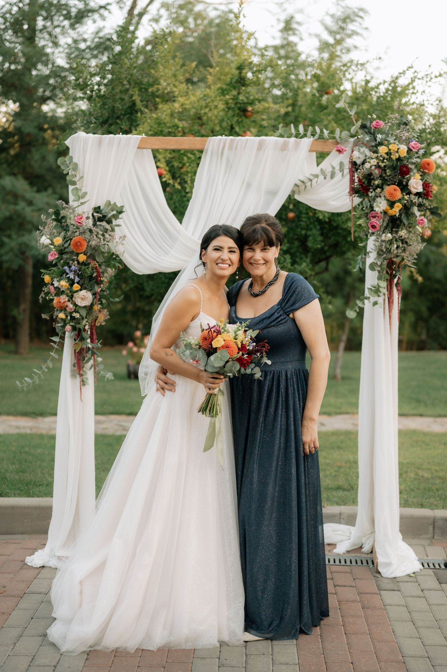 Wedding ceremony setup with white draped fabric arch decorated with coral and peach floral arrangements in an outdoor garden setting.
