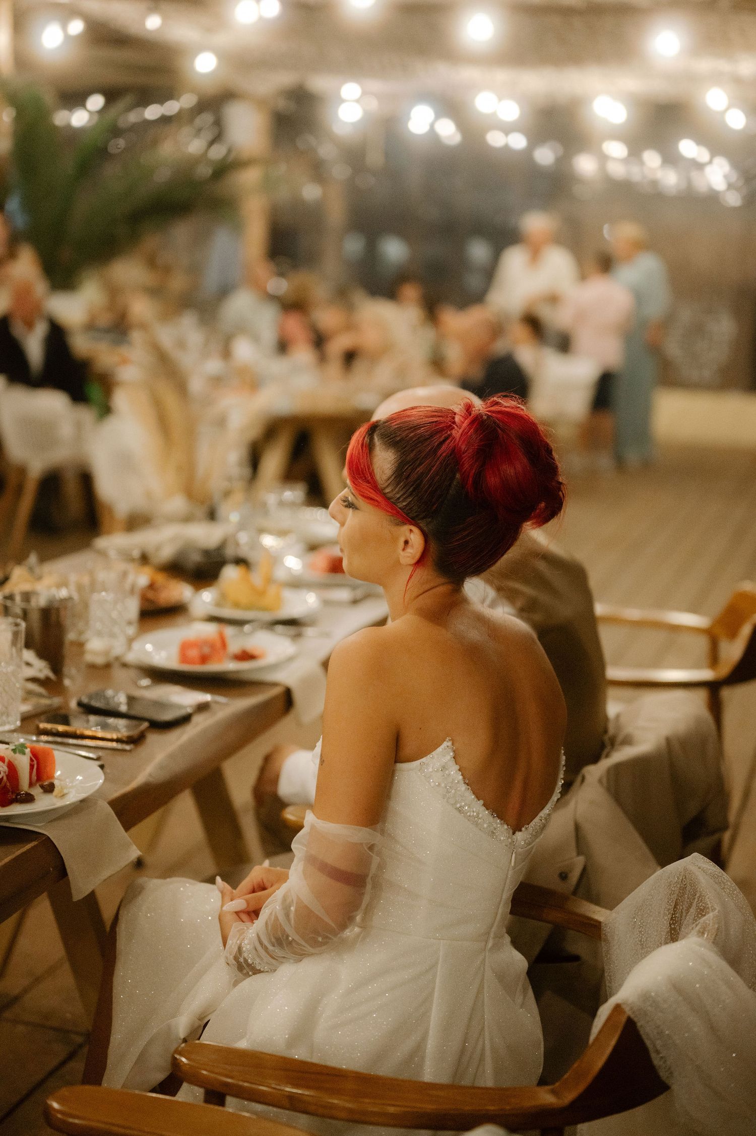 A bride in a white wedding dress sits at an elegantly decorated reception table in warm ambient lighting.