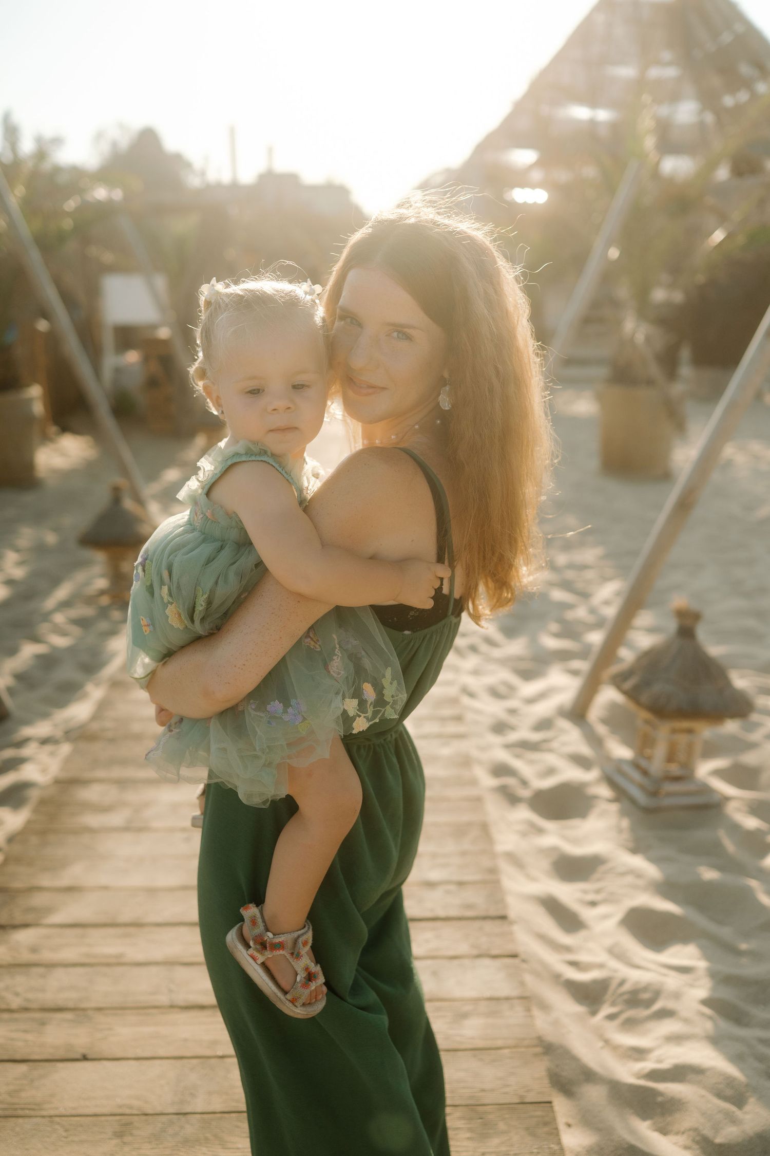 A mother and child share tender moments together on a sandy beach boardwalk at sunset.