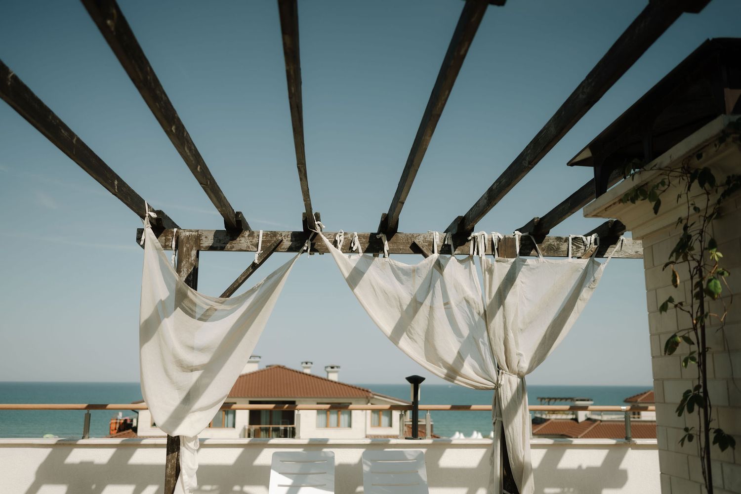 White curtains blow in the breeze along a beachfront resort with ocean views and palm trees in the background.
