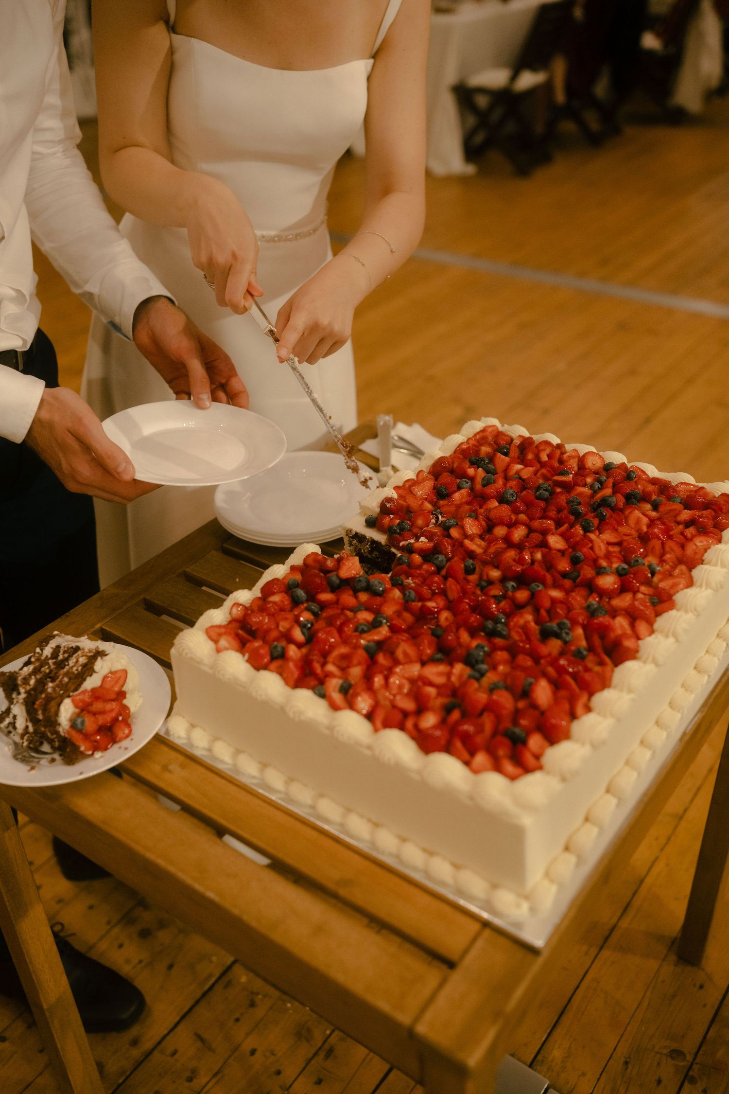A series of photos showing a white wedding cake being decorated with fresh strawberries and blueberries on a wooden table.