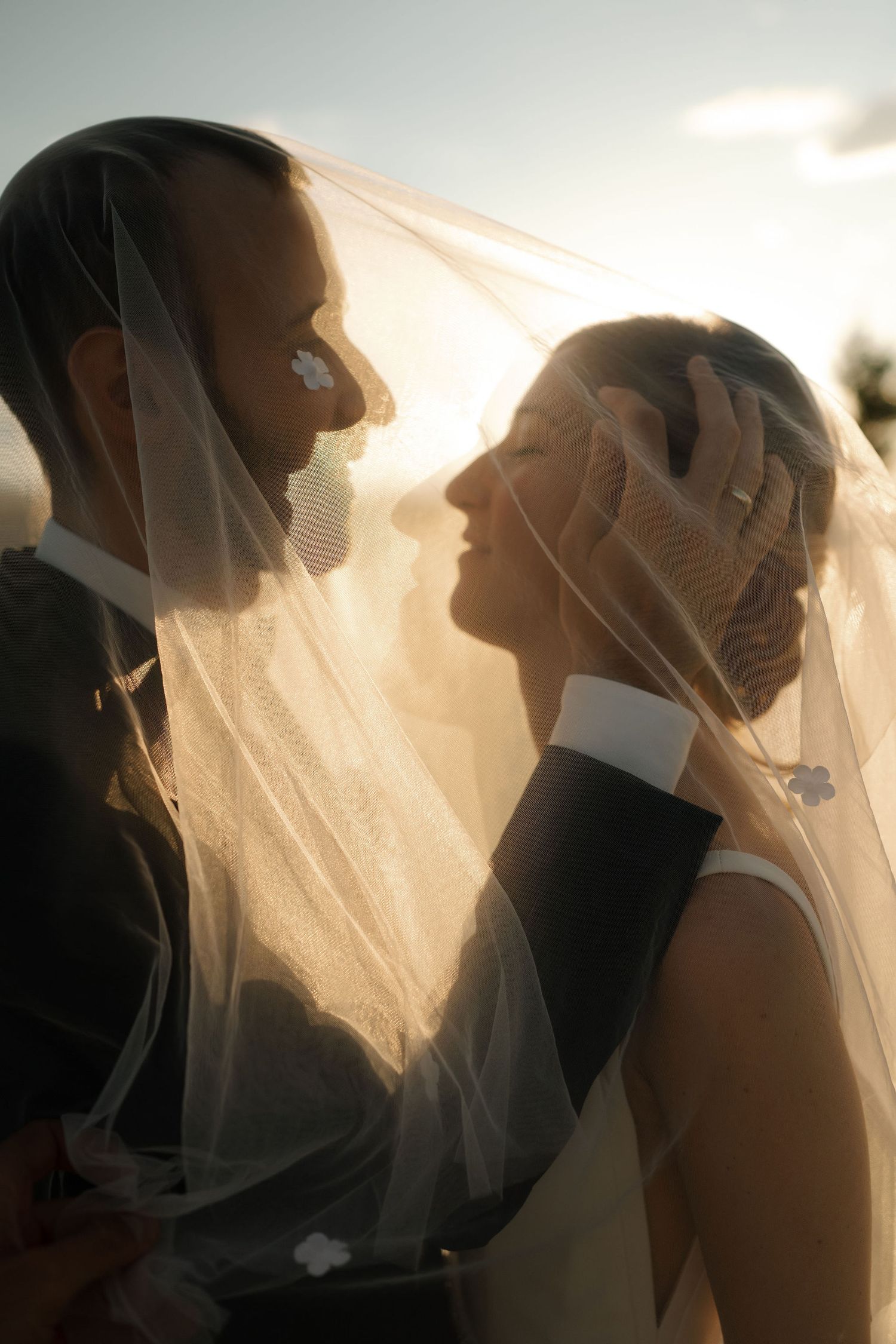 A romantic wedding moment captured through a sheer veil at sunset with soft lighting creating an intimate silhouette.