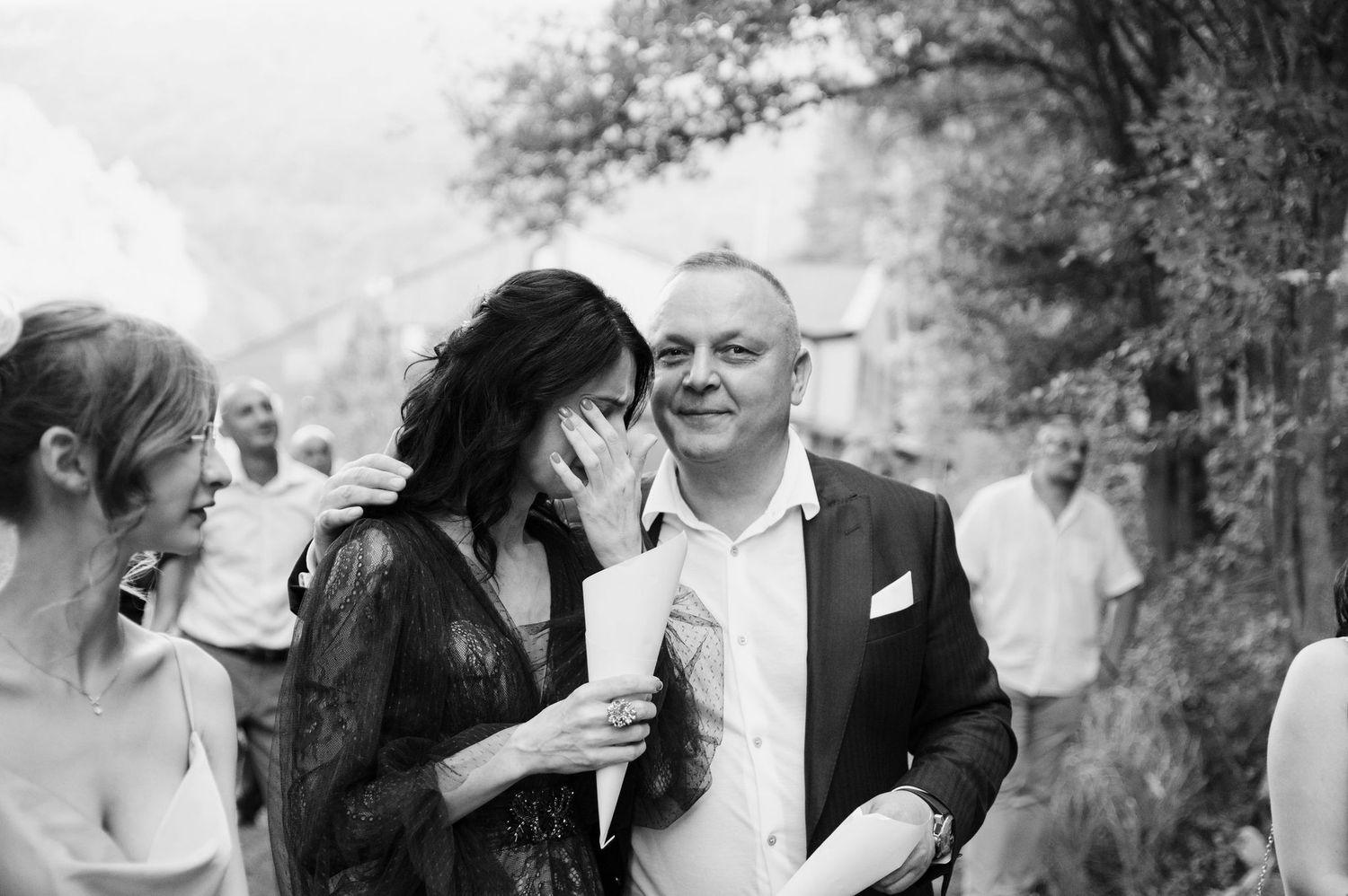 Black and white photo of wedding guests mingling in an outdoor forest setting.