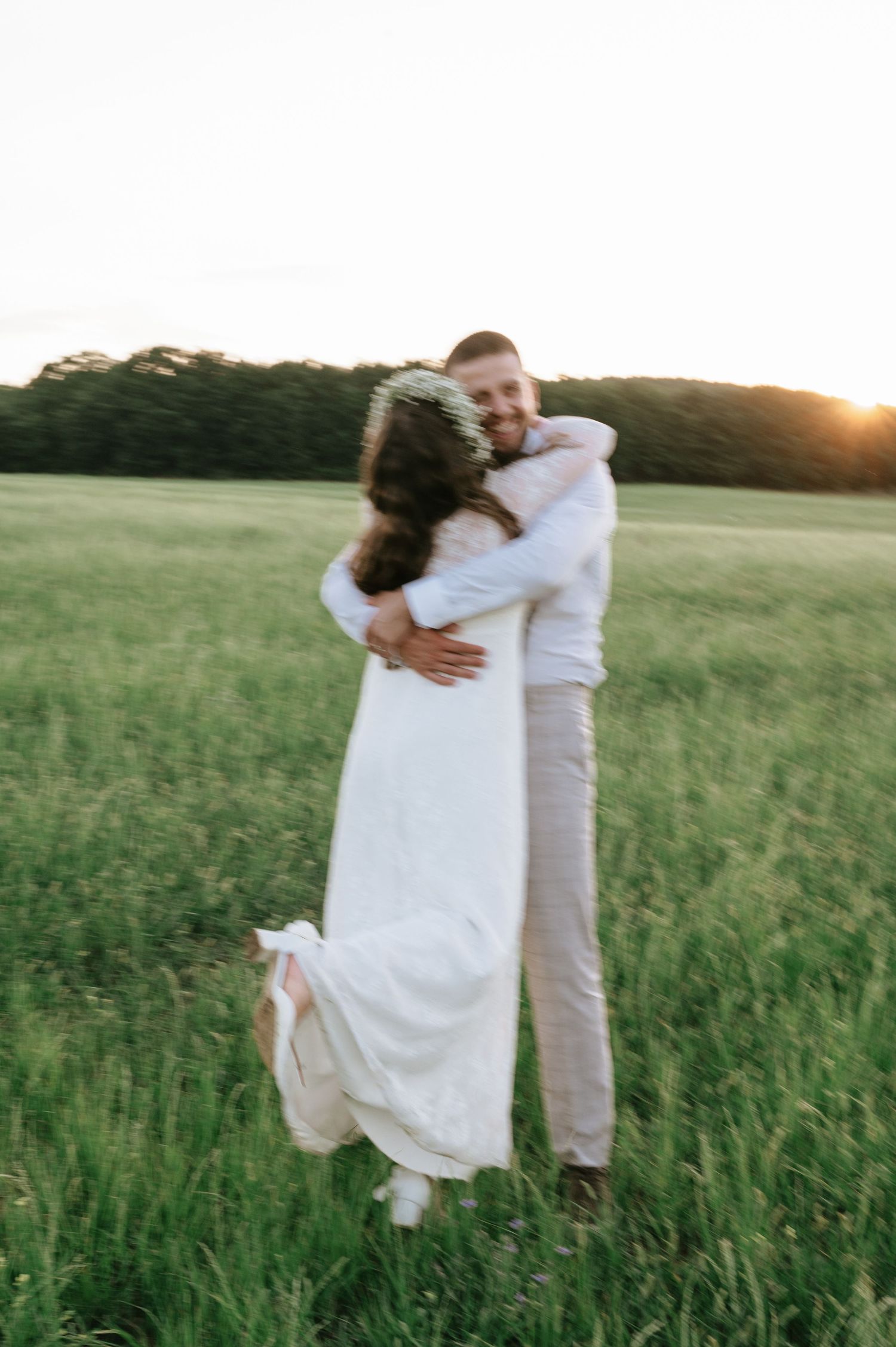 A couple embraces in a sunlit field of tall grass during a romantic photoshoot at golden hour.