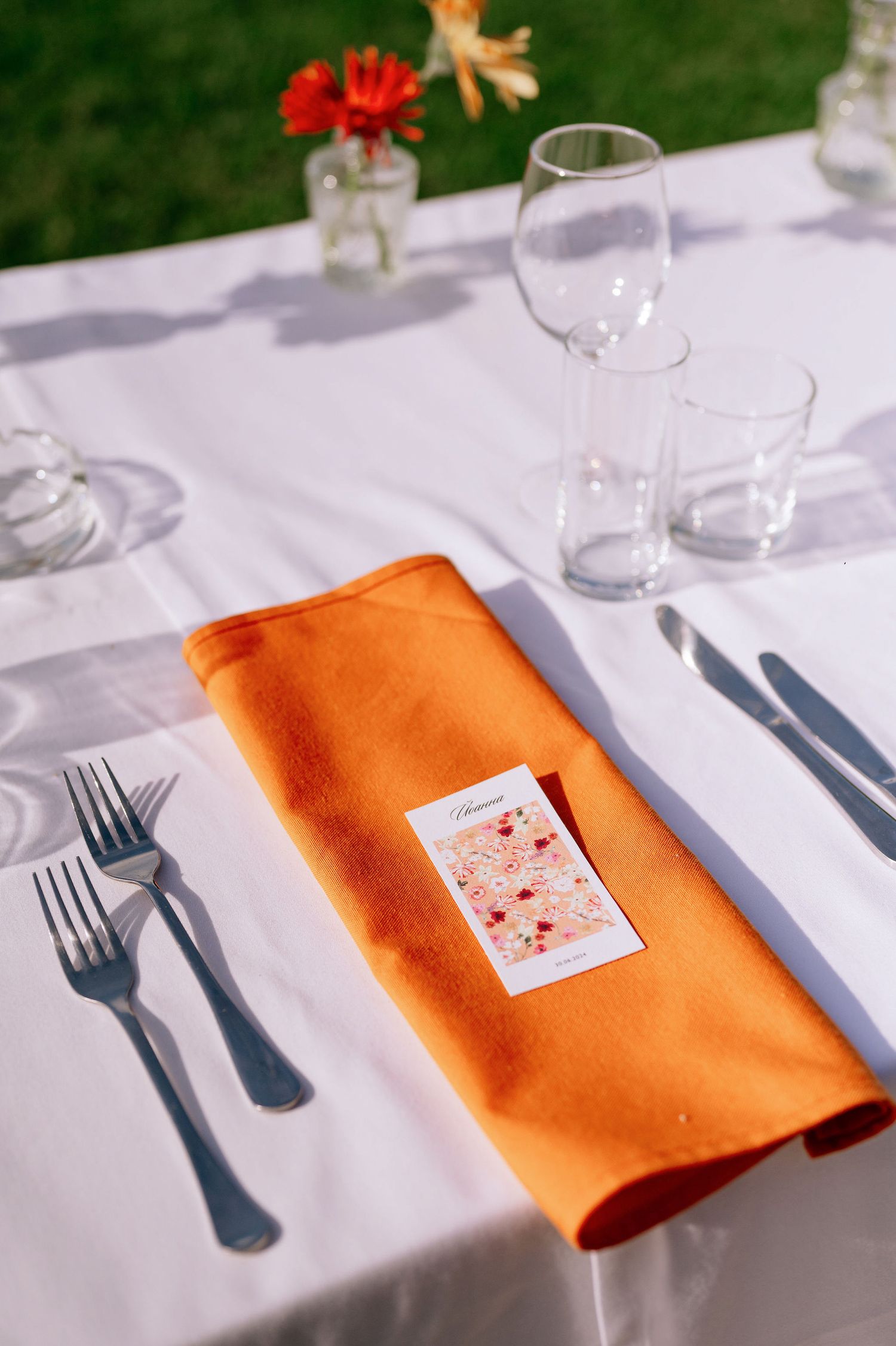 Table setting with bright orange napkin and place card on crisp white tablecloth.