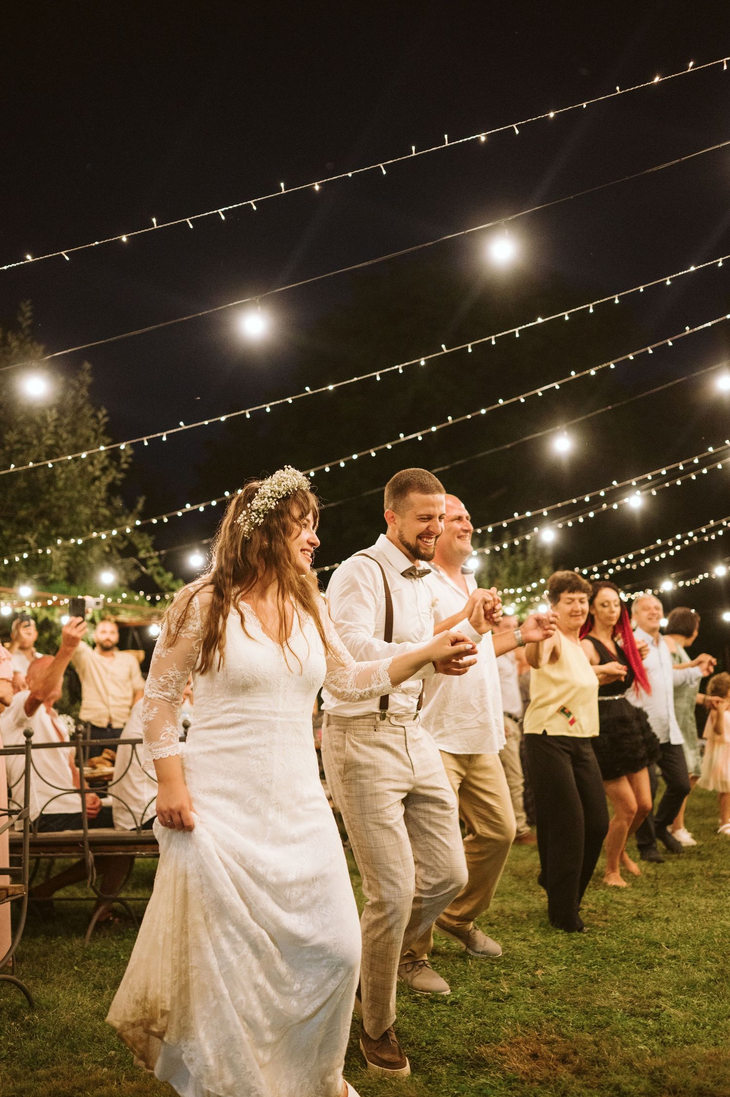 Wedding couples dancing together under romantic string lights at outdoor evening reception.