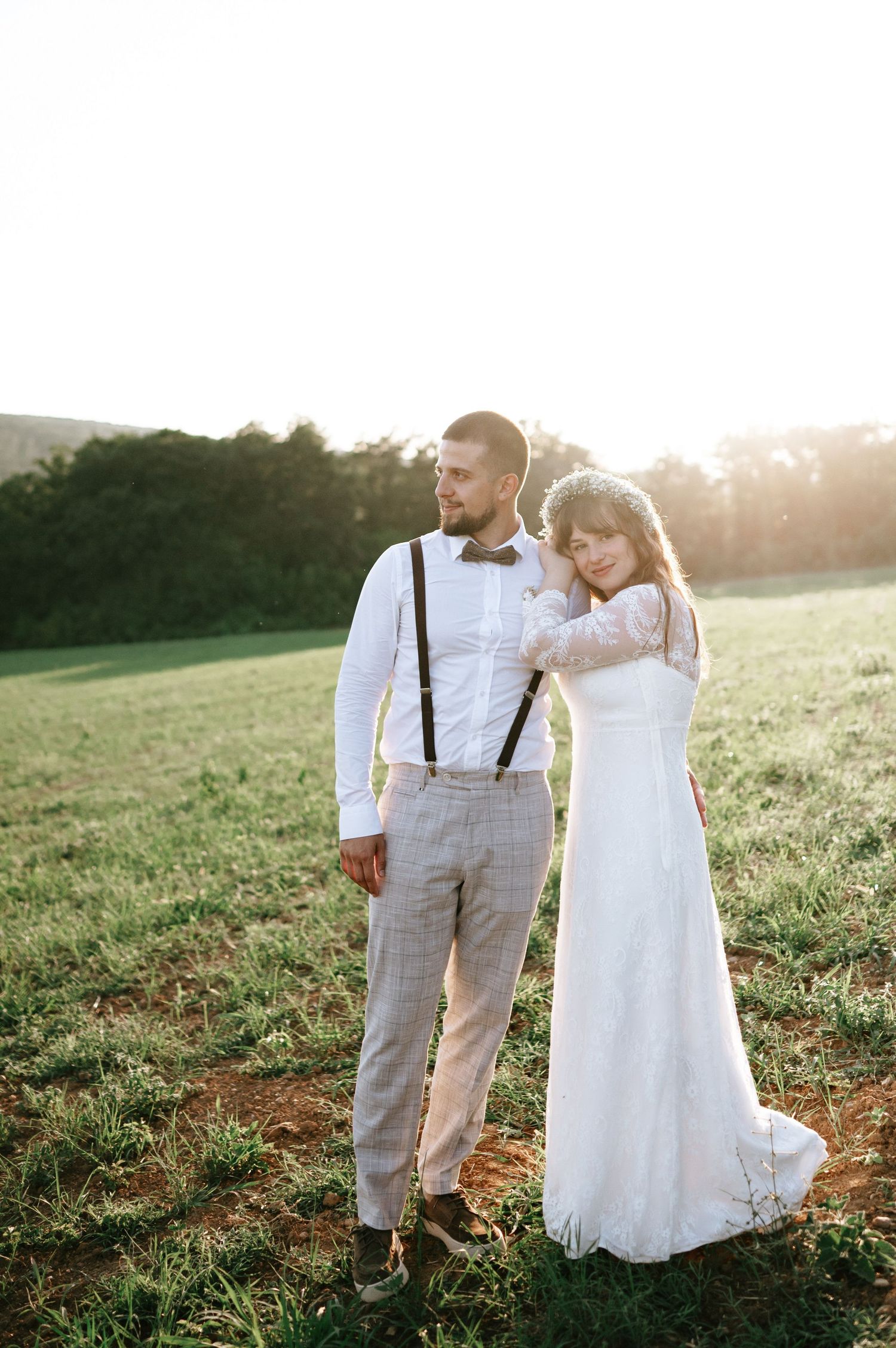 Wedding couple poses playfully in a grassy meadow at sunset.