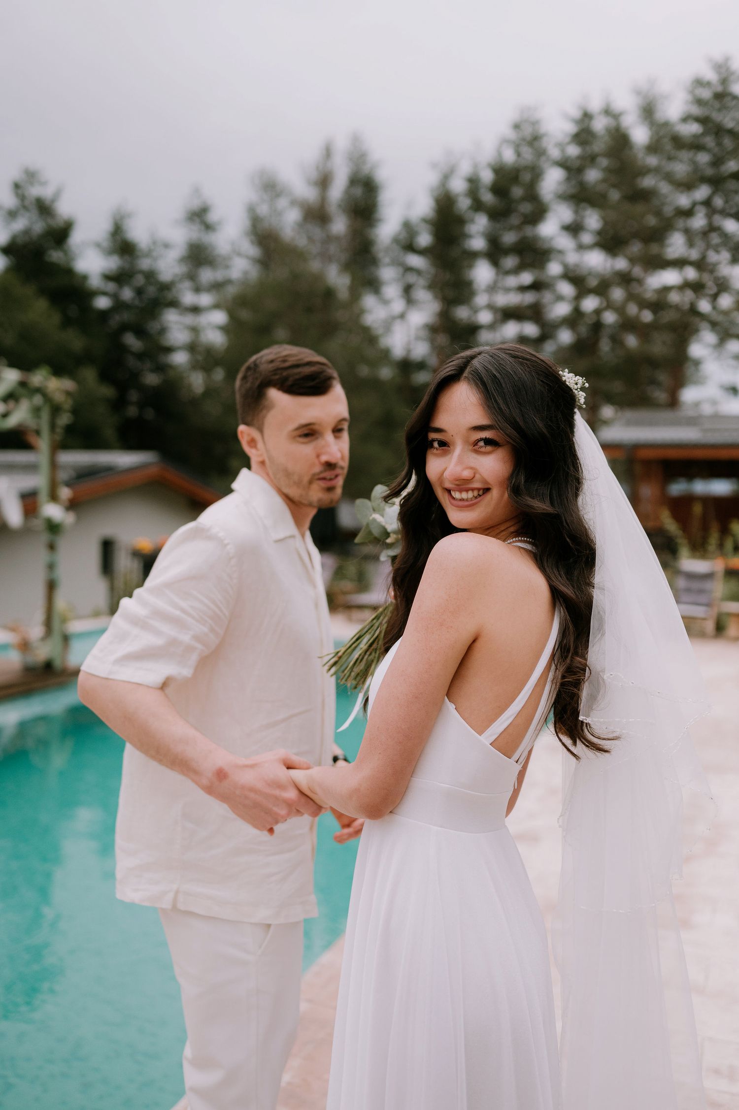 A romantic wedding photoshoot by a turquoise pool with the couple in white attire dancing and twirling.