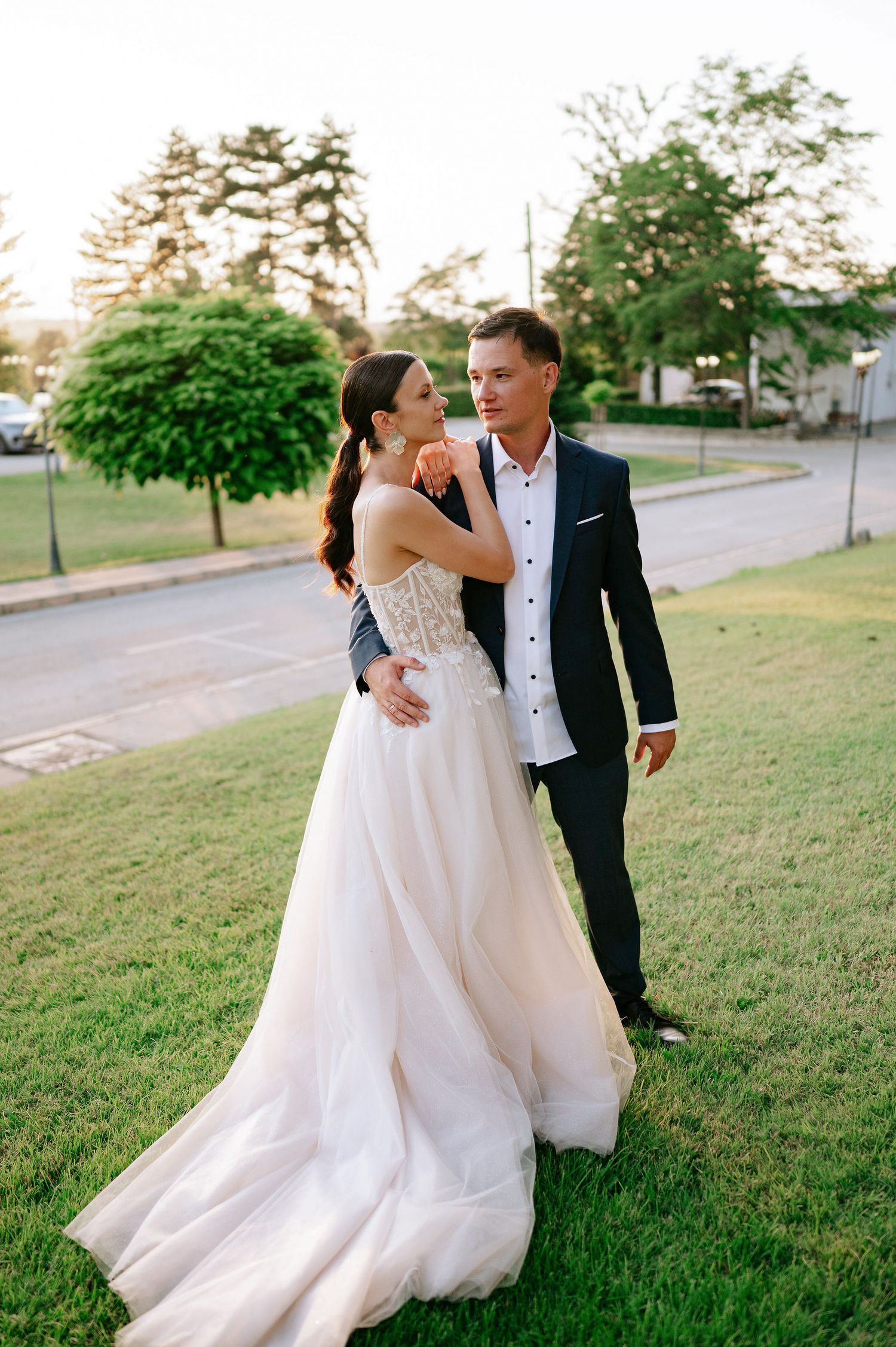 Wedding couple dances playfully on a grassy hillside at sunset.