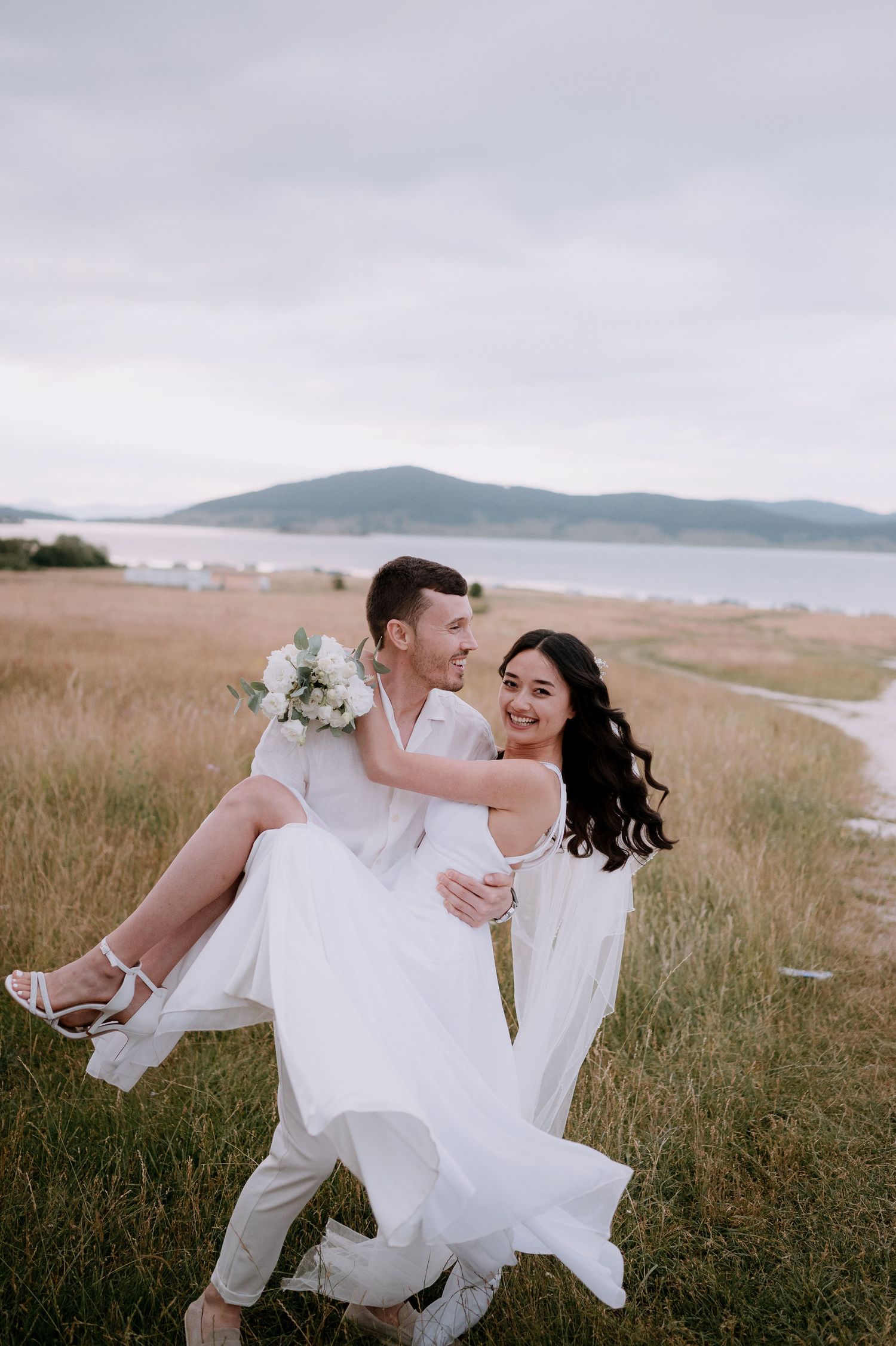 Candid wedding moment showing a playful dance lift in a scenic grassland setting.