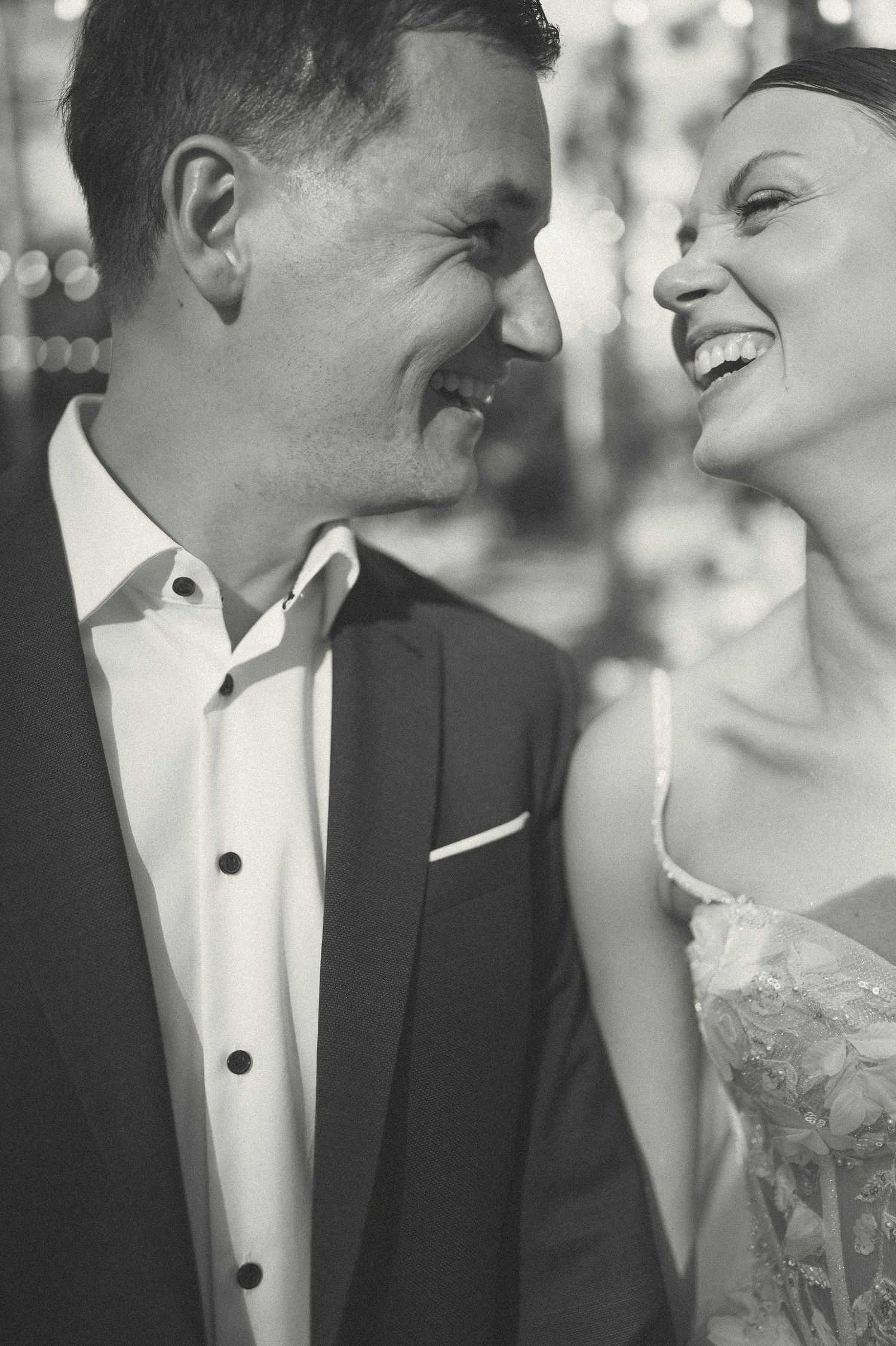 Black and white intimate portrait of newlyweds sharing a candid laughing moment.