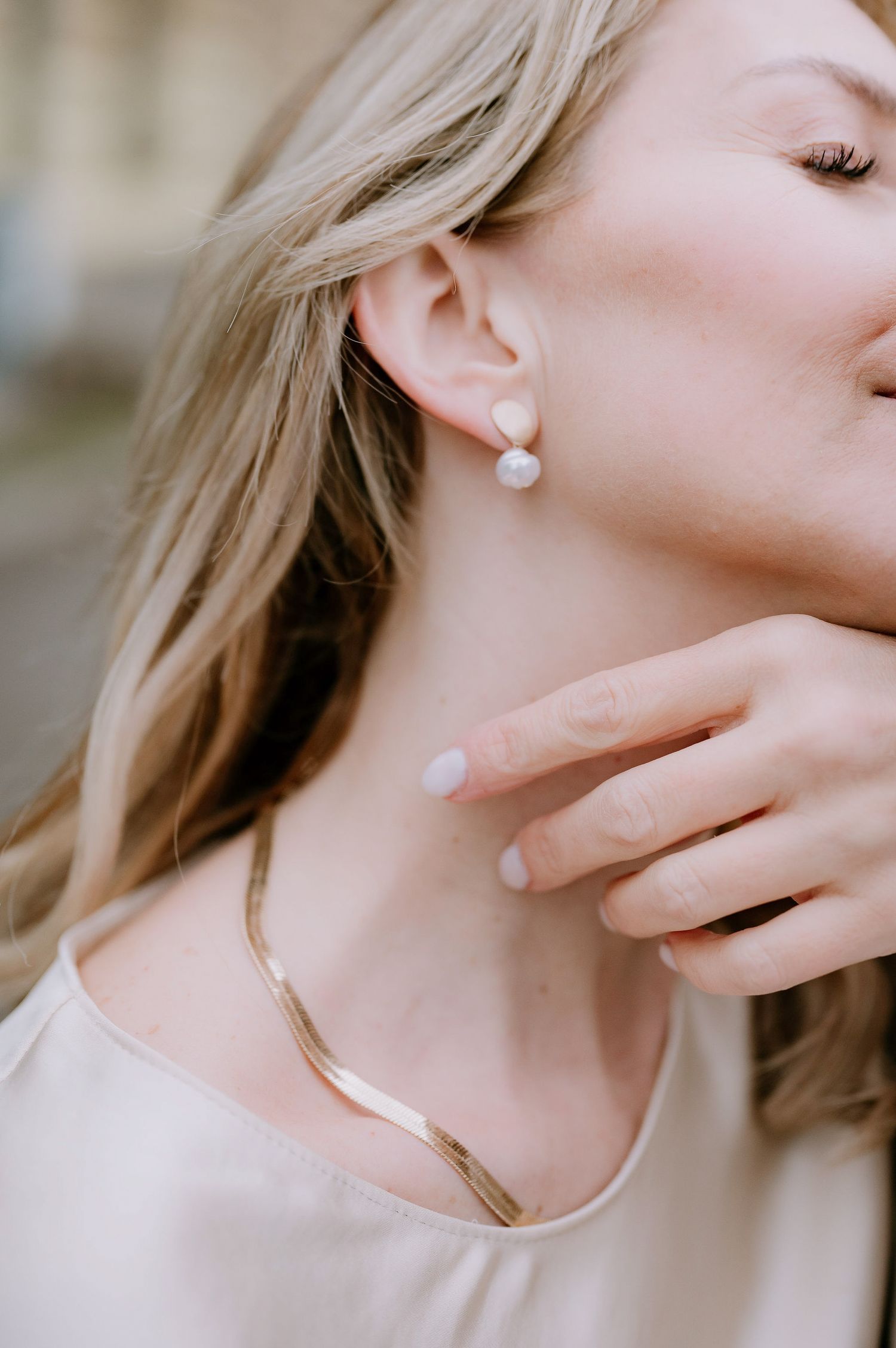 Elegant gold jewelry details including necklace and pearl earrings on neck and ear.