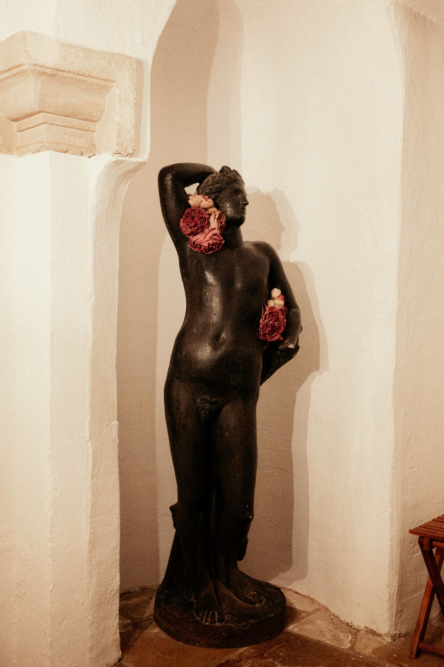 A black decorative torso sculpture with red flowers displayed against a white wall.