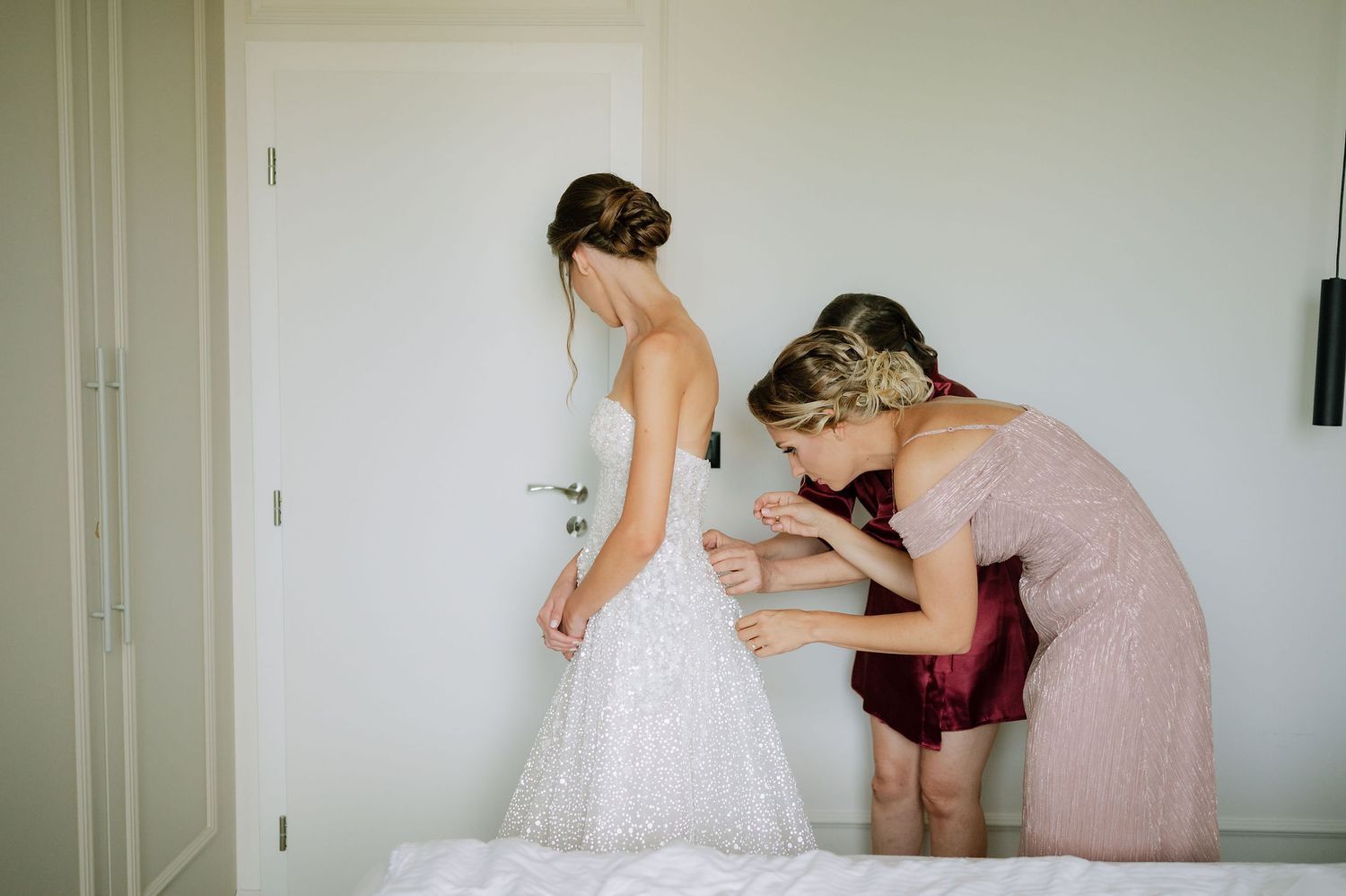 Wedding dress being fitted with assistance in a bright room.