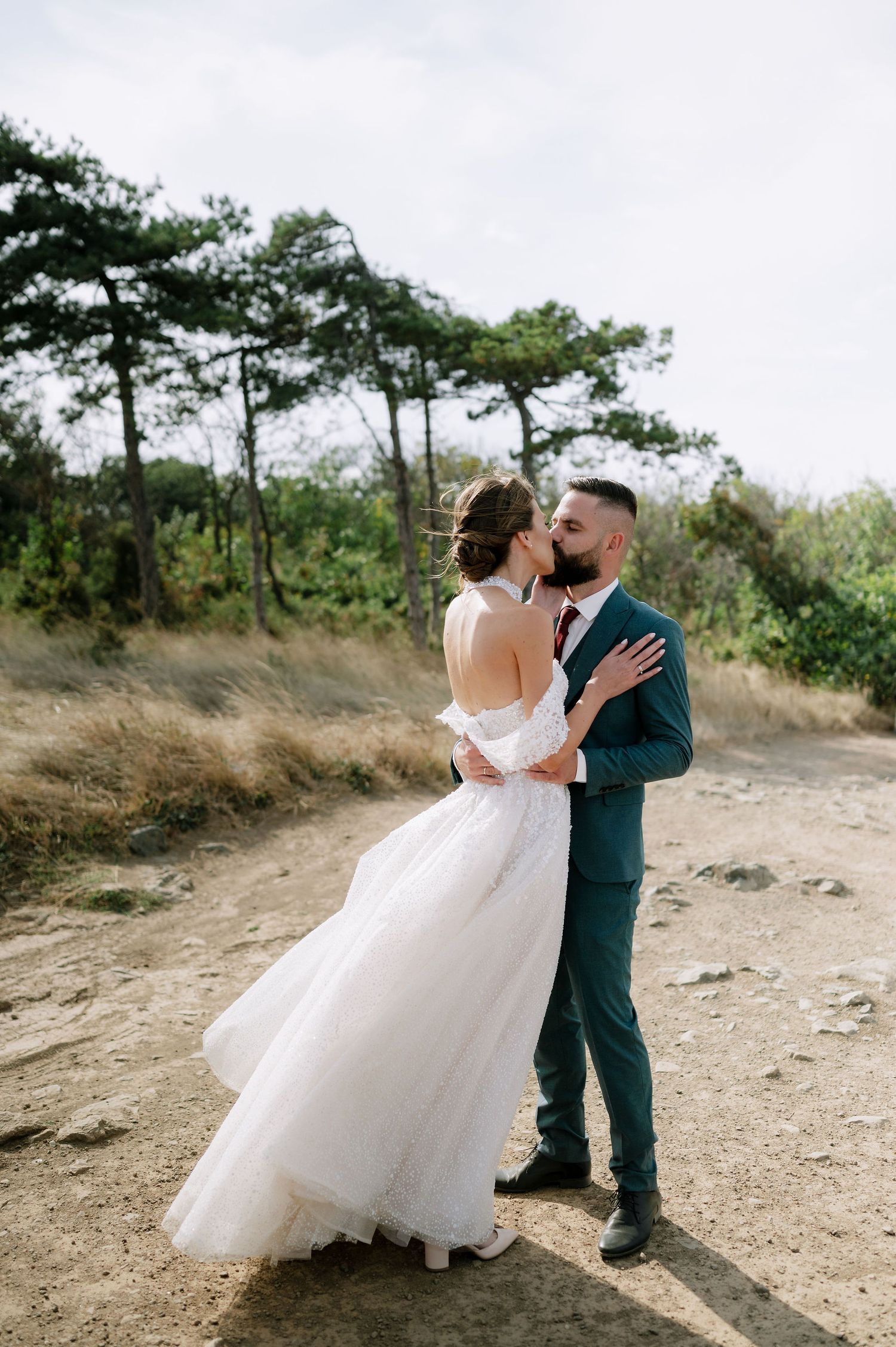 Wedding couple shares romantic moment on dirt path surrounded by natural landscape.