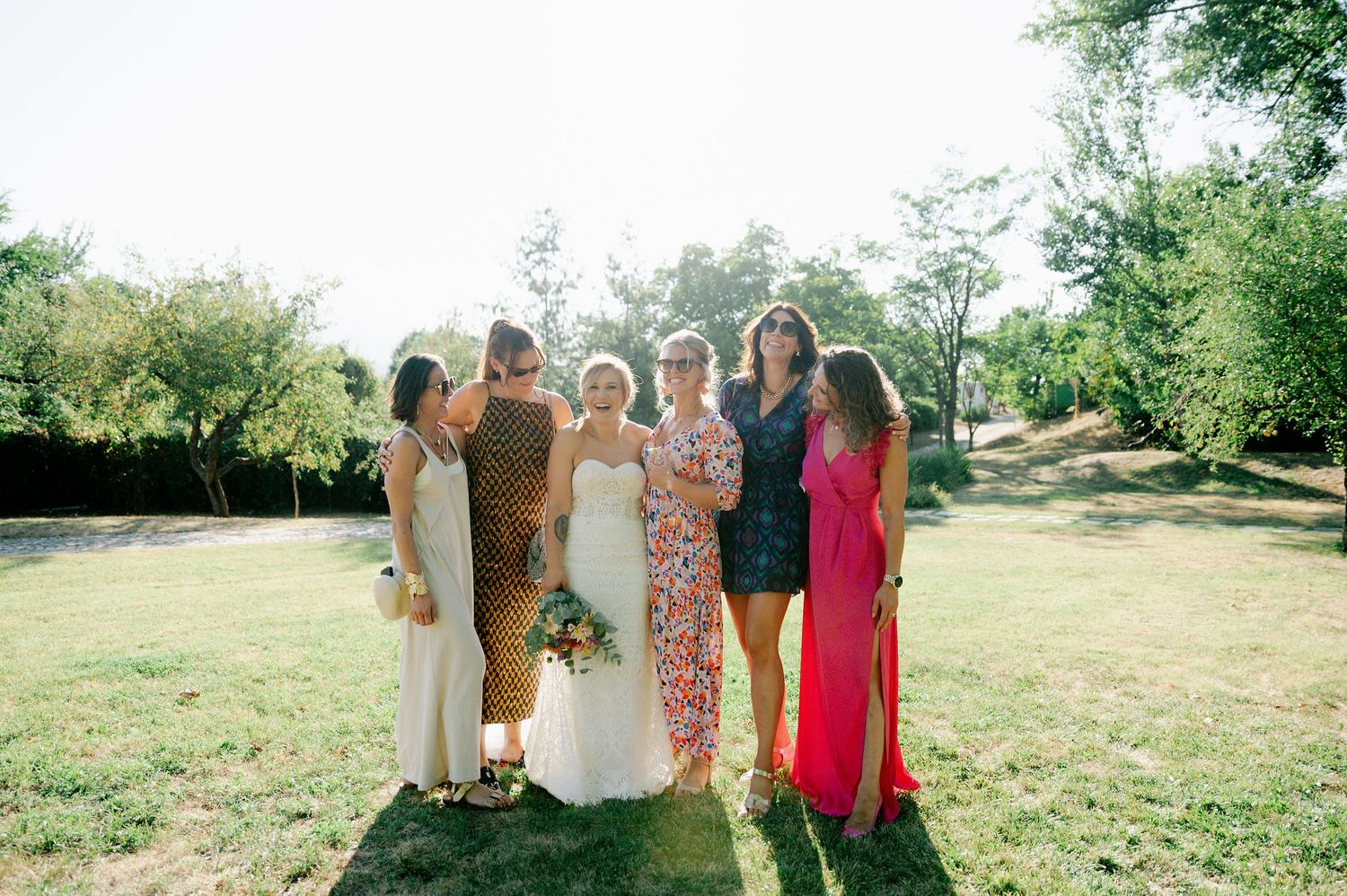 Wedding party members pose together in a line on a grassy hillside.