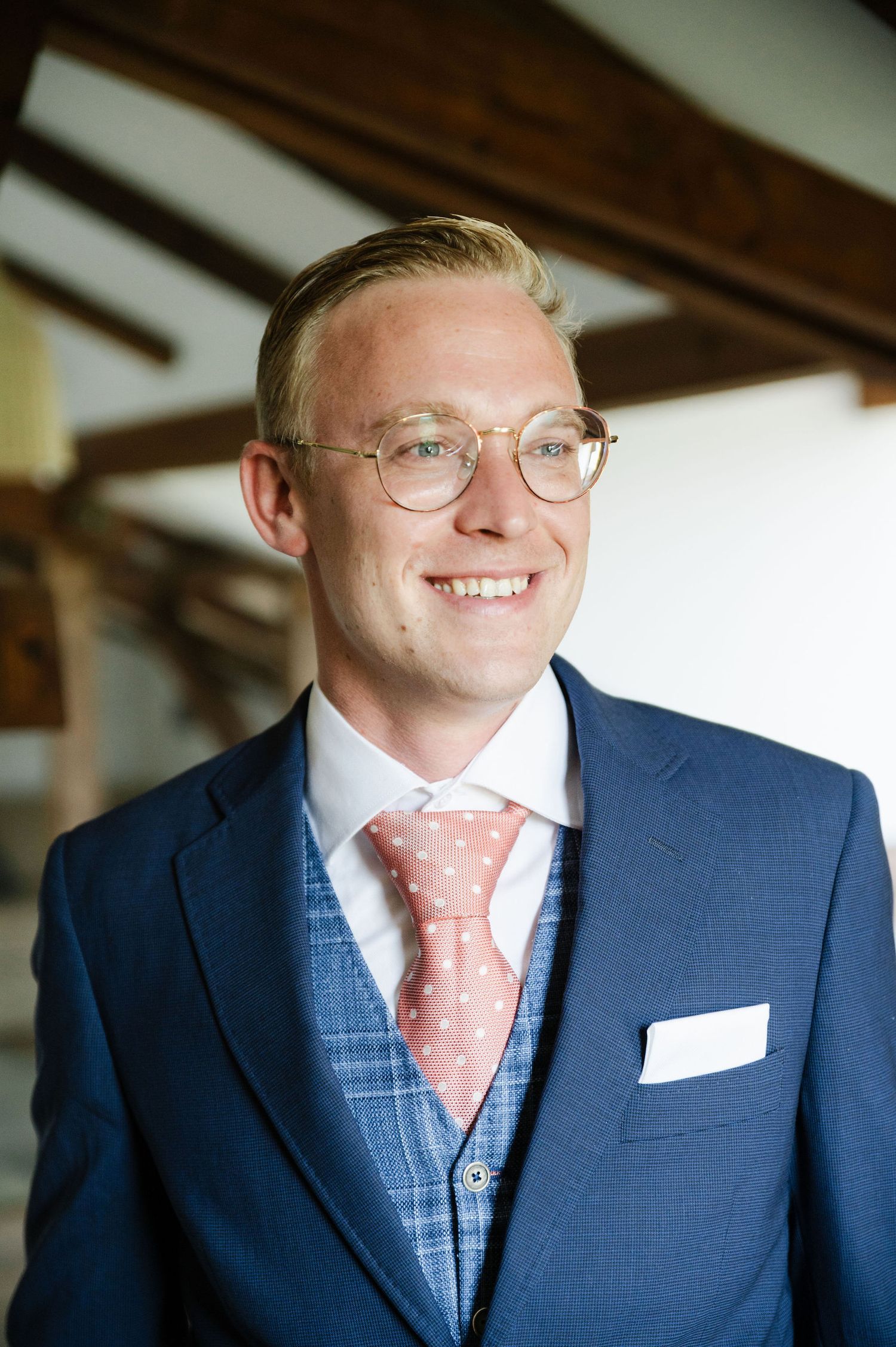 Person in a navy suit and pink polka dot tie smiling in natural light.