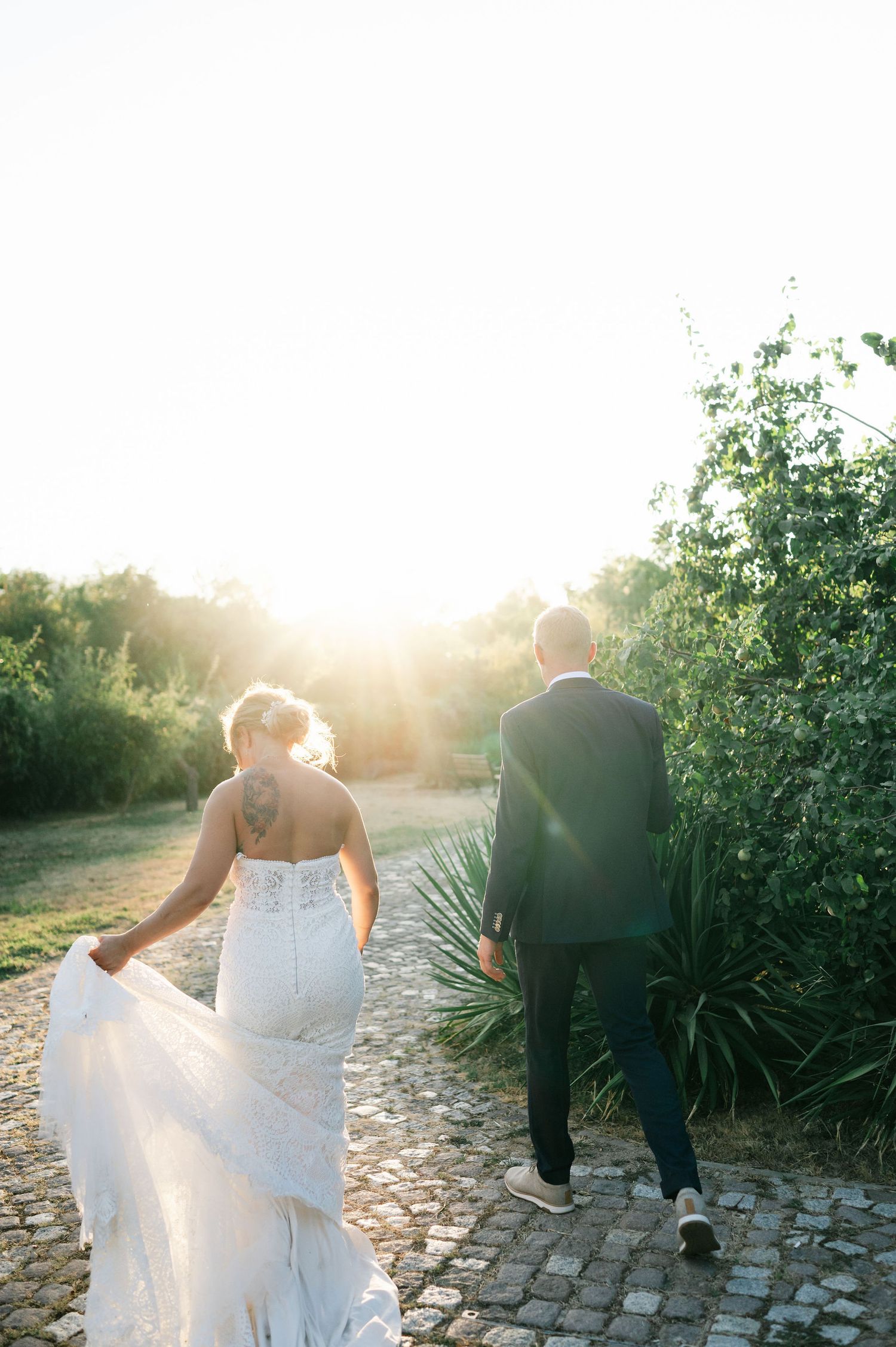 Wedding couple walking along cobblestone path during golden hour photoshoot.