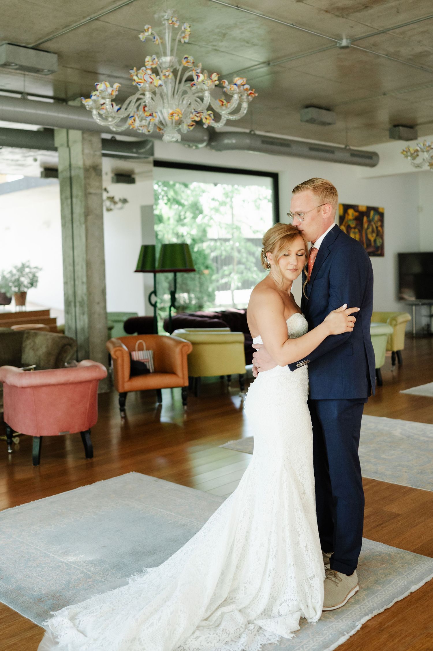 A tender dance moment captured in a modern venue with elegant chandeliers and large windows.