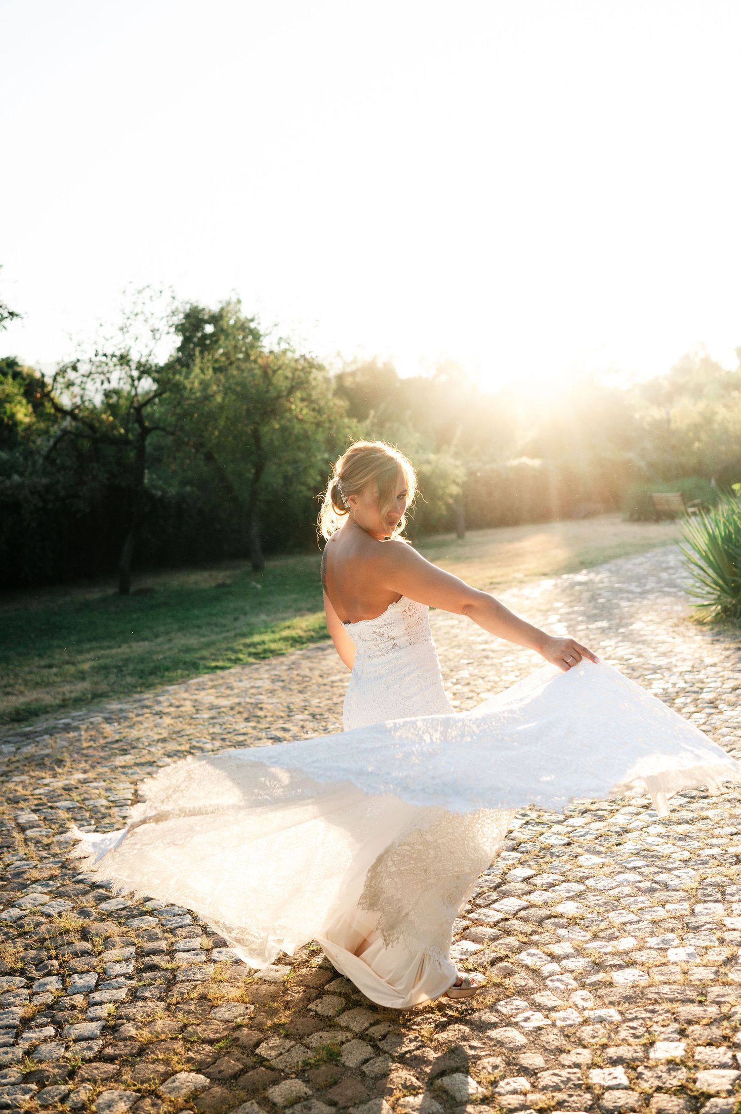 Elegant wedding dress movement captured in warm sunlight on stone pathway.