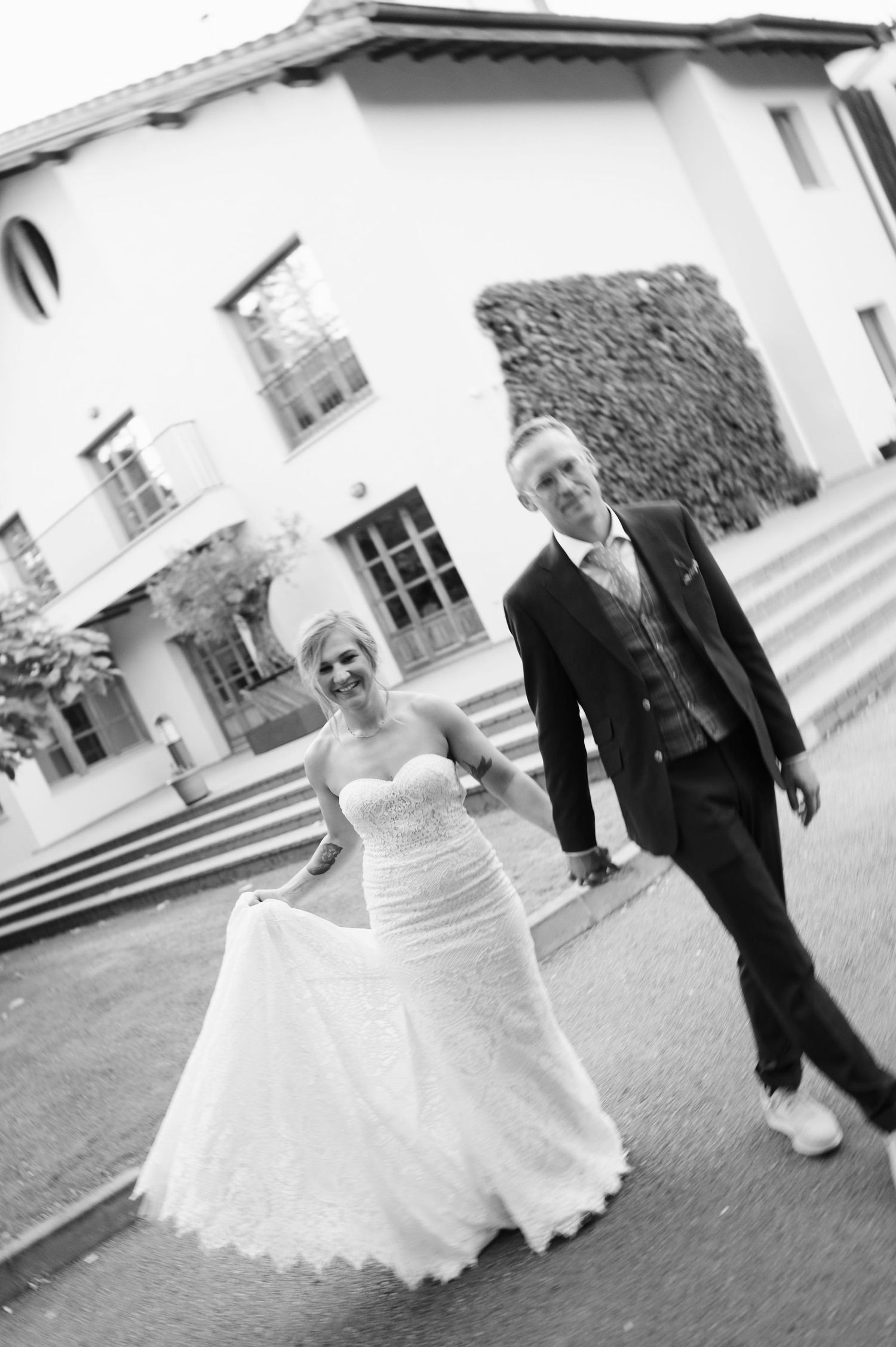 Black and white wedding photo of couple dancing outside elegant white villa.