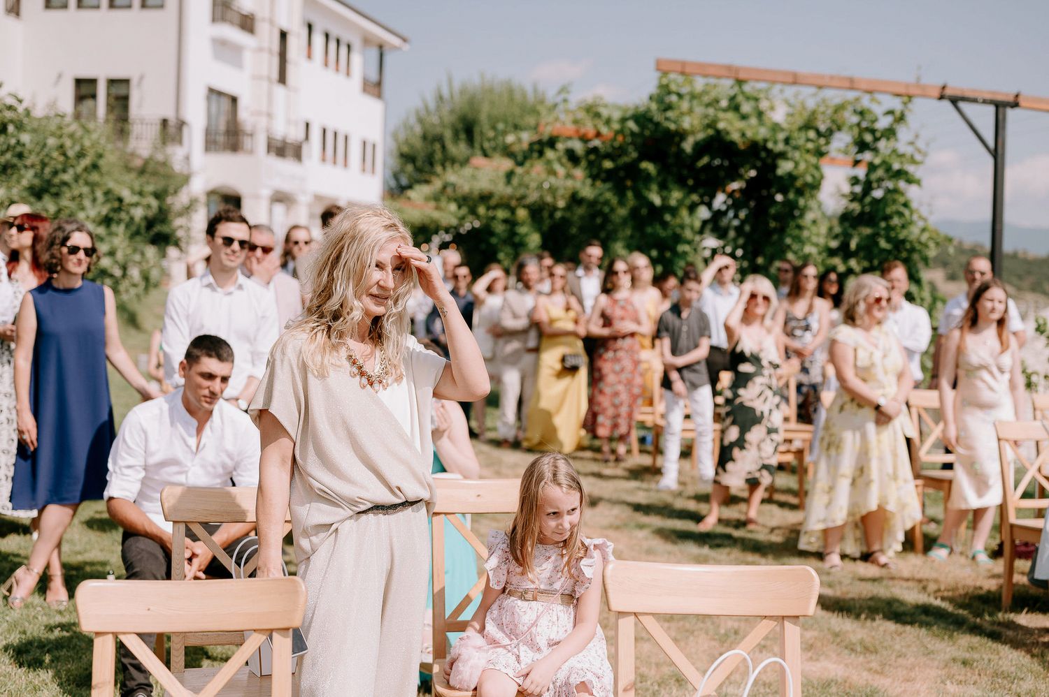Outdoor wedding reception with guests seated at long wooden tables under sunny skies.