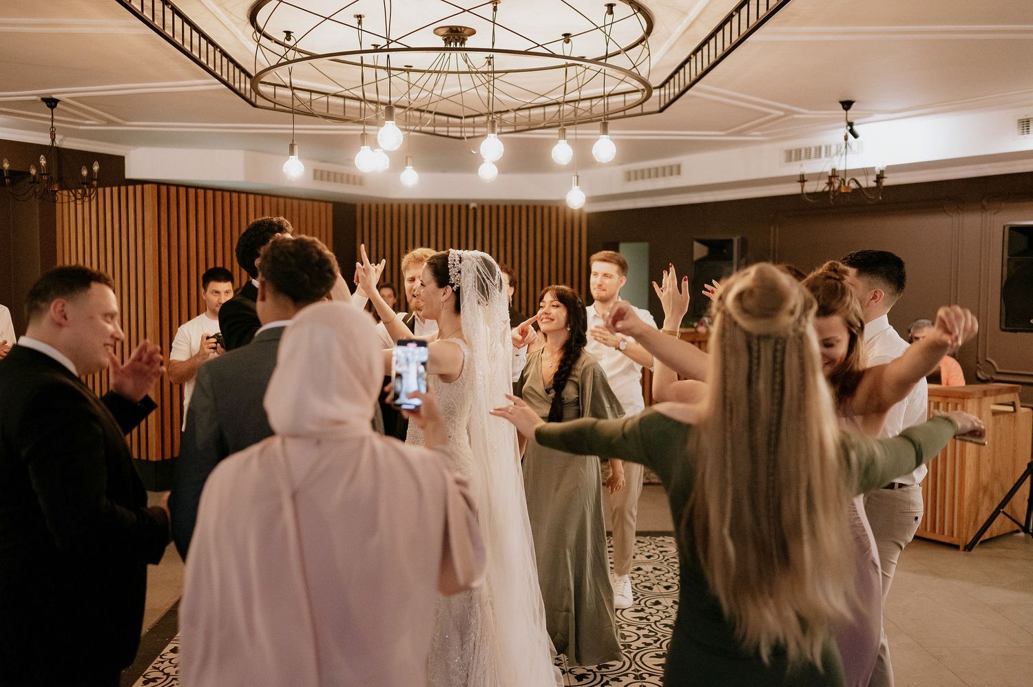 Wedding reception venue with elegant chandelier and dancing guests.