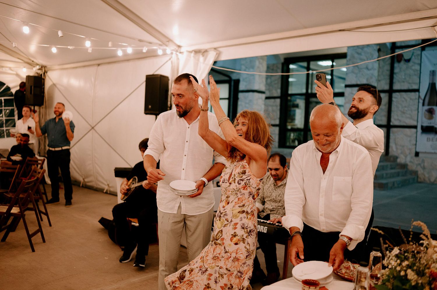 Guests enjoying a lively celebration under string lights in an elegant white tent venue.