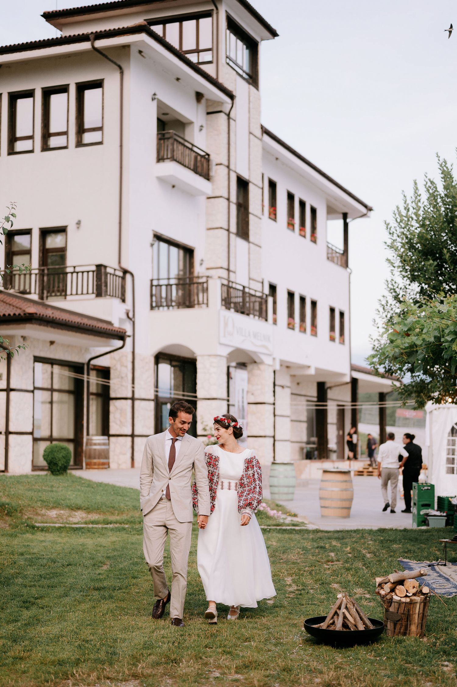 Wedding celebration outside a white Mediterranean-style building with a bonfire setup.