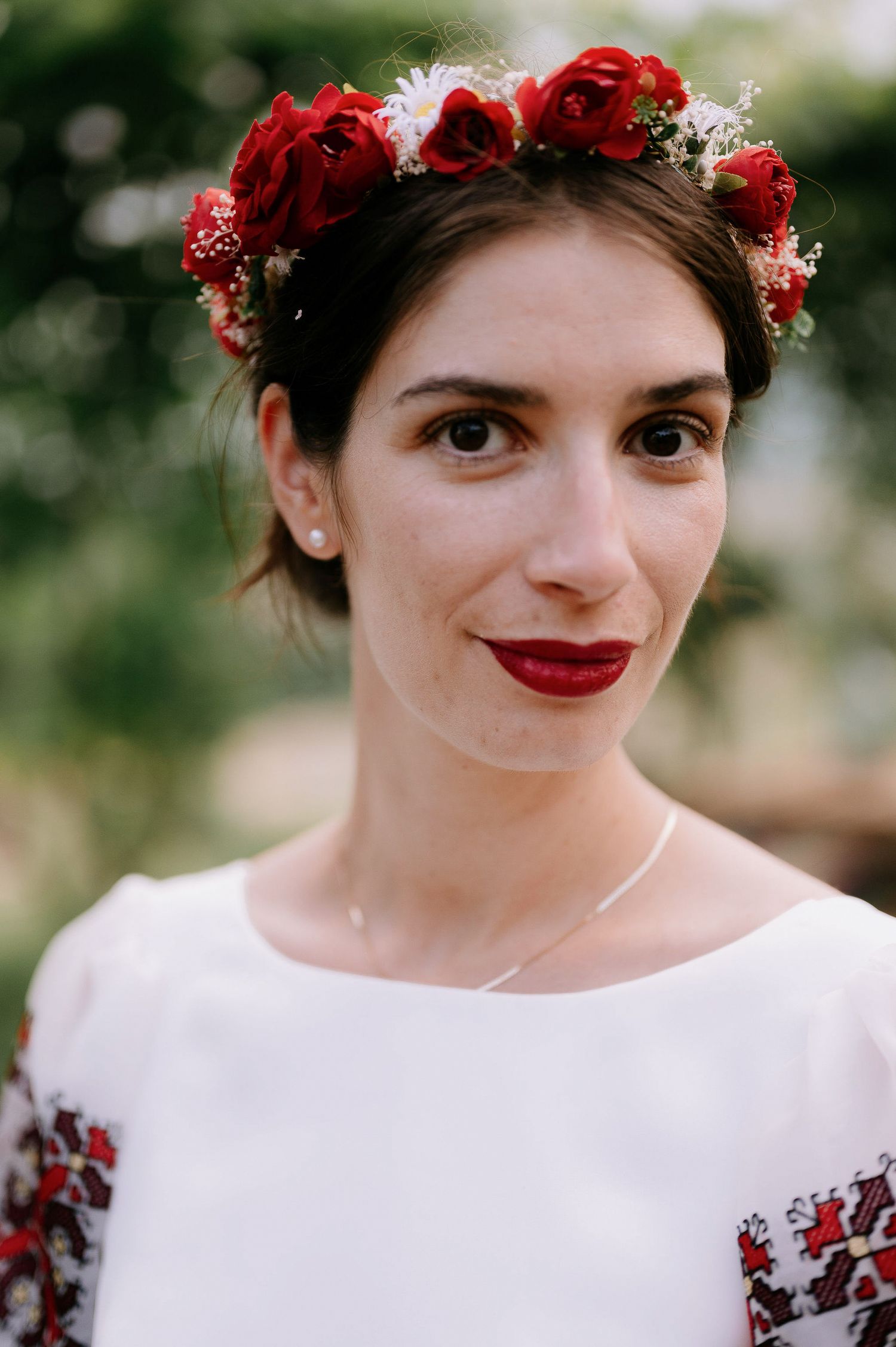 Close-up portrait featuring red lipstick, floral crown and white embroidered dress.