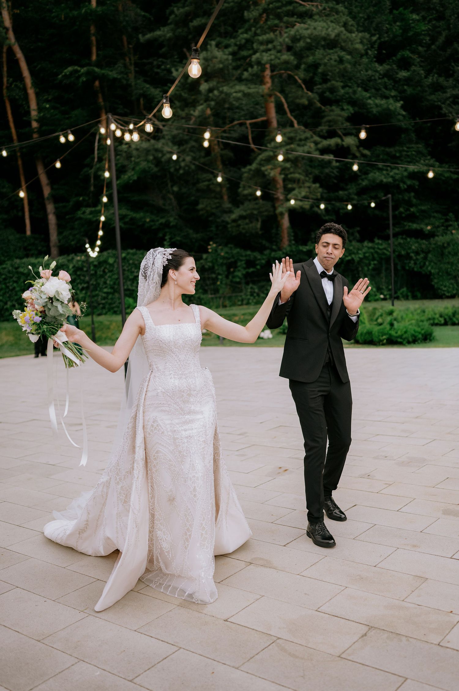 A couple dancing joyfully on a stone patio with string lights overhead.