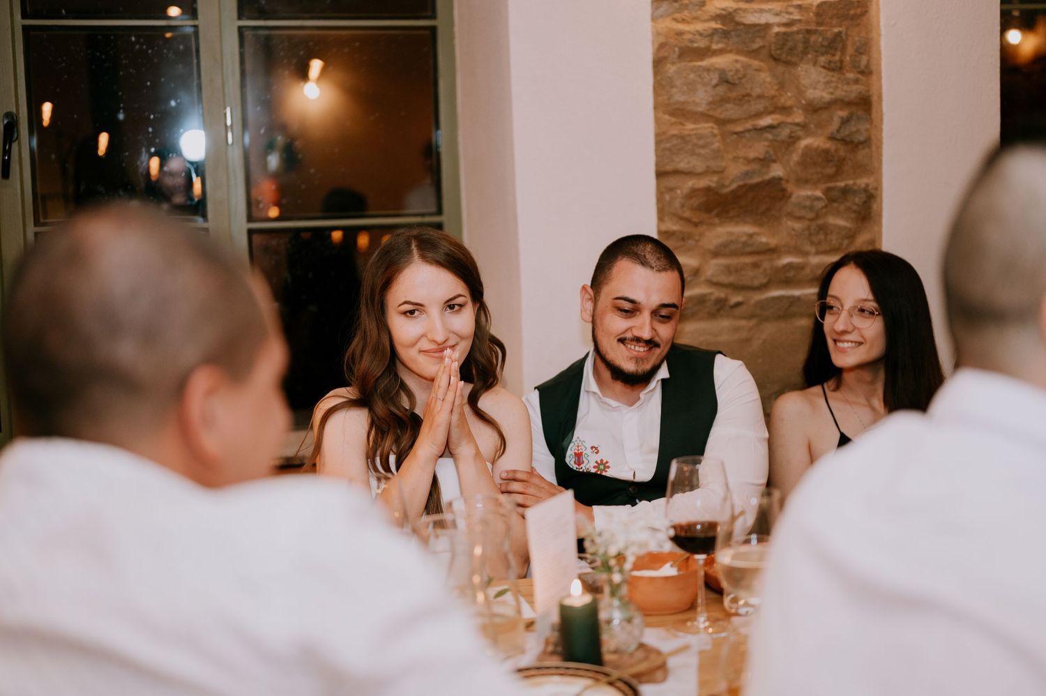 Celebratory dinner gathering with guests seated at long tables in a rustic venue.