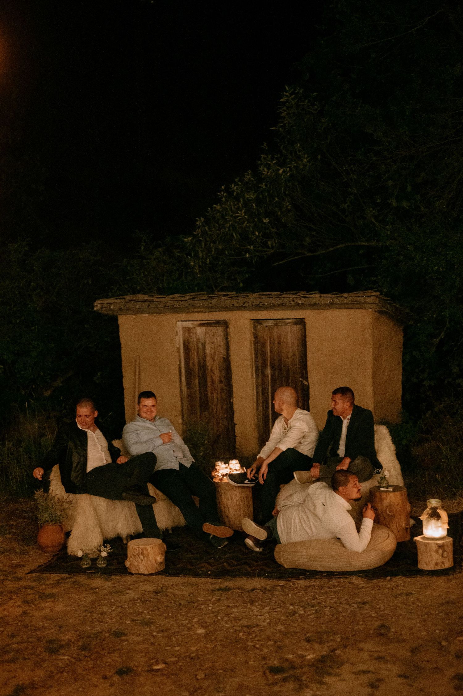 Wedding guests relaxing on blankets outdoors at night by candlelight.