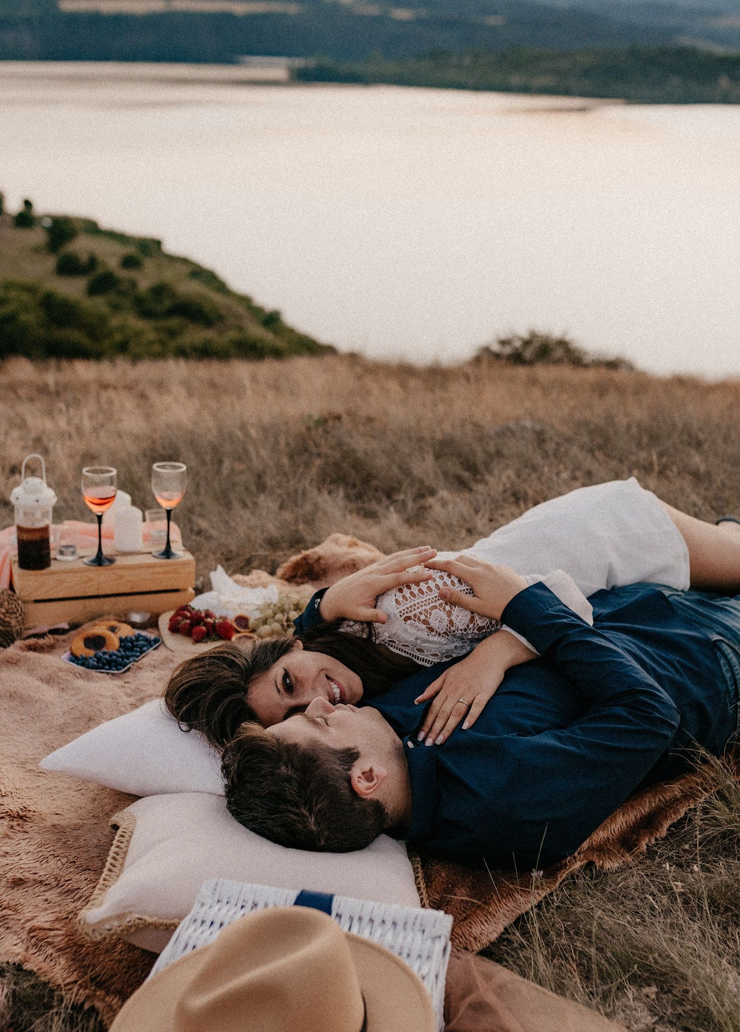 Scenic lakeside picnic setup with couple resting on blanket at dusk.