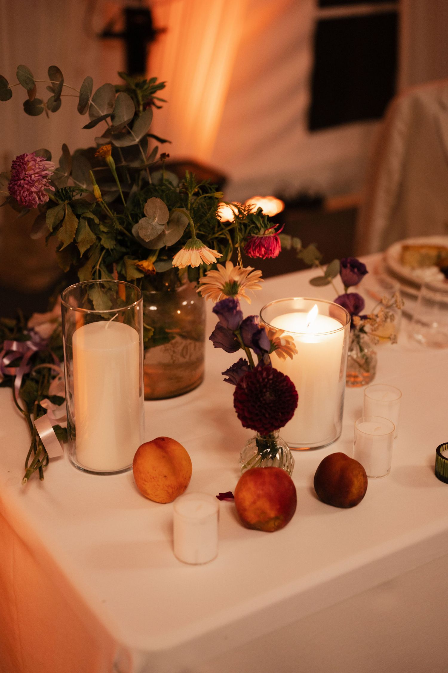 Elegant table decor with white candles and purple flowers in small vases creating a romantic ambiance at a dinner setting.