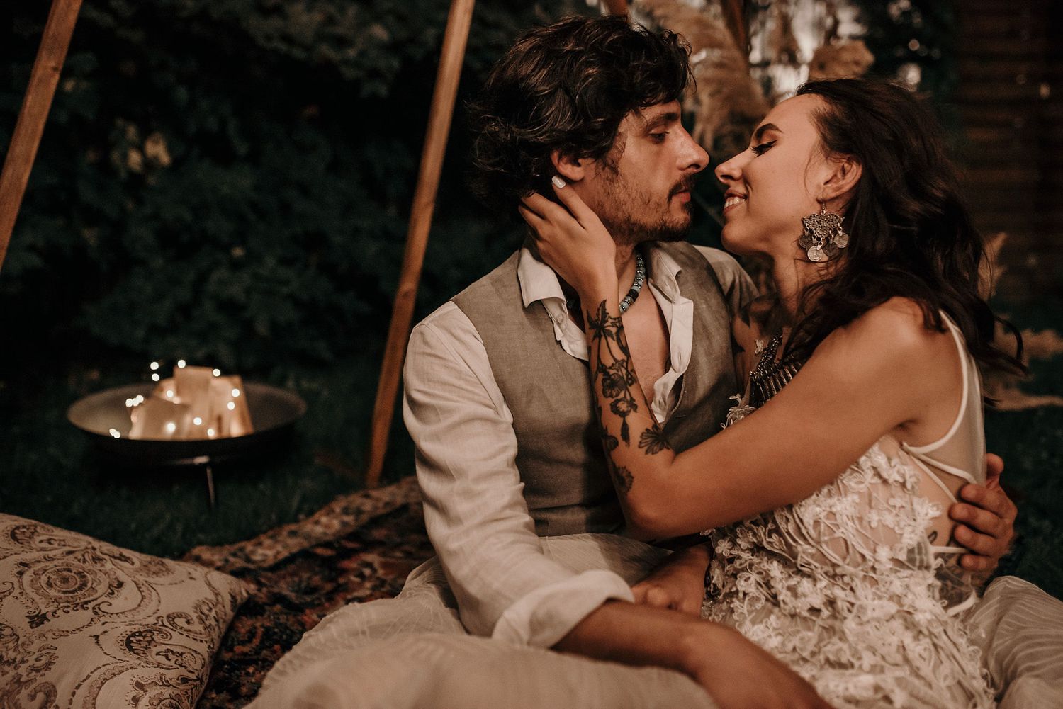 A romantic wedding couple shares intimate moments in a rustic outdoor setting at dusk.