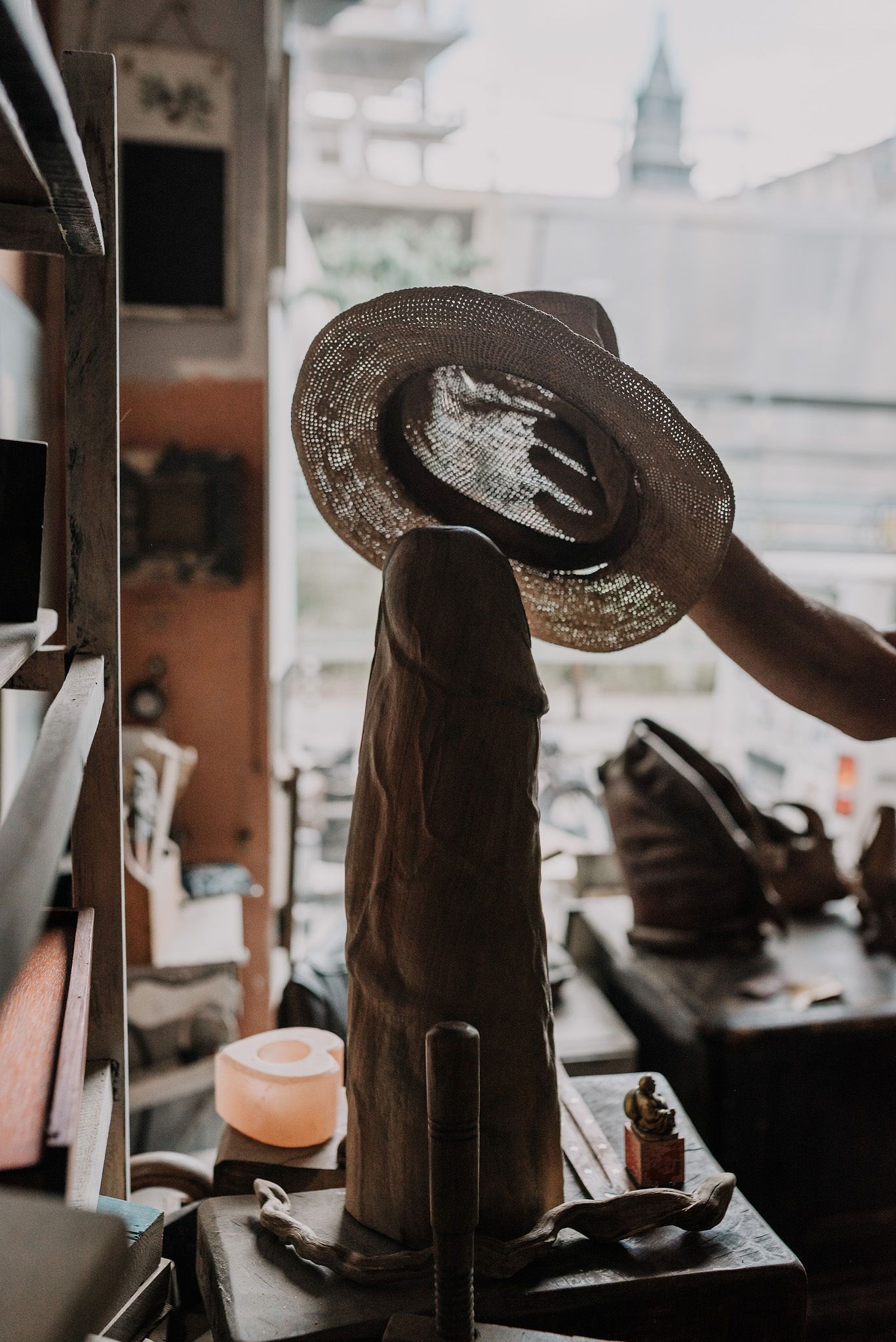 A rustic cowboy hat sits on display against a window with a church spire visible outside.