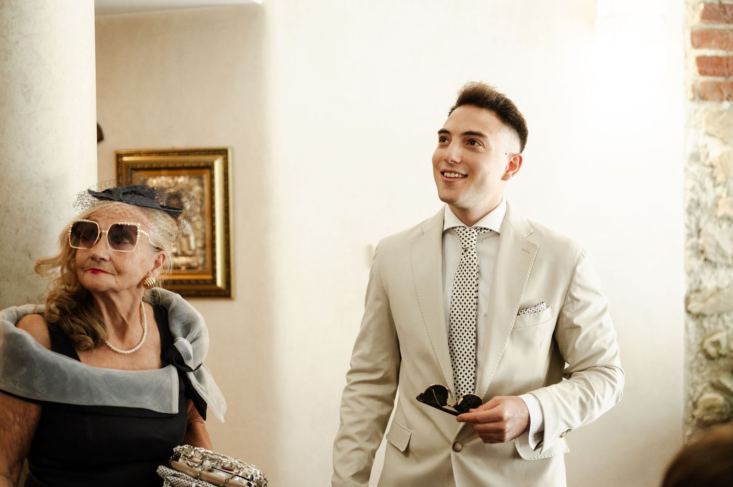 Wedding guests in formal attire share laughs in an elegant indoor setting.